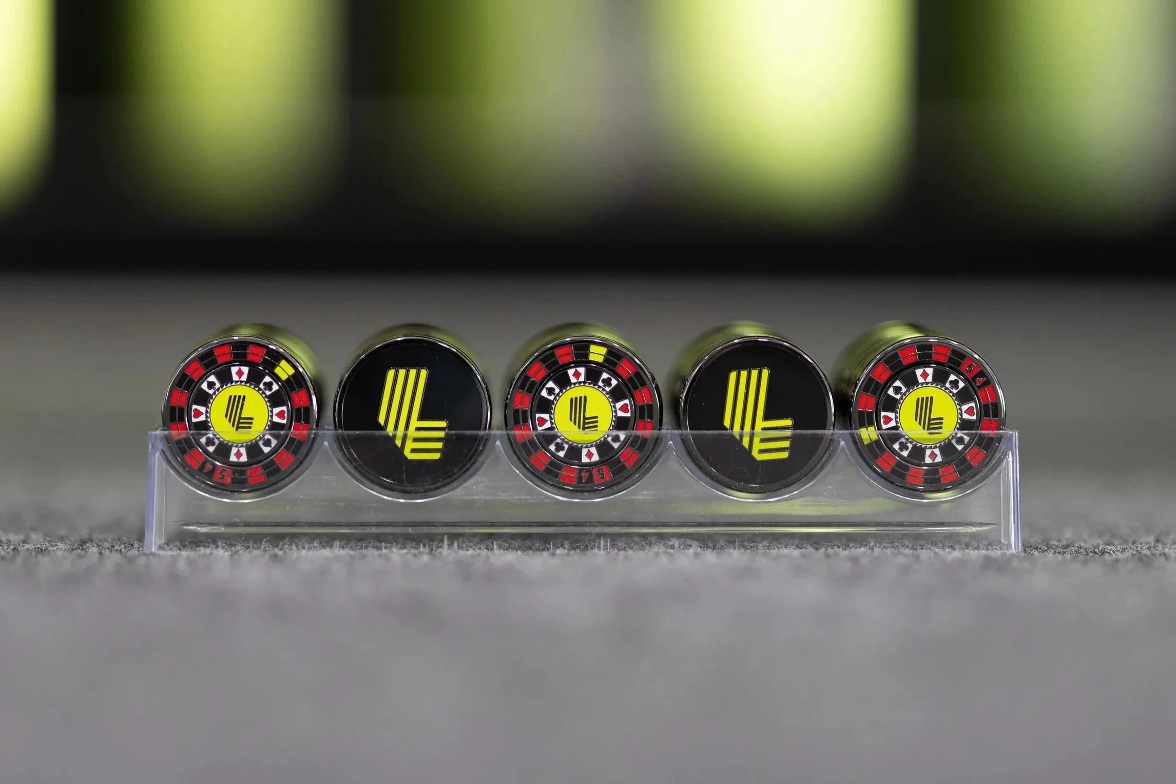 Five casino chips with black, red, yellow, and white designs, placed in a row in a plastic stand. Four chips have the number 4, and one chip has a yellow 'L' symbol.