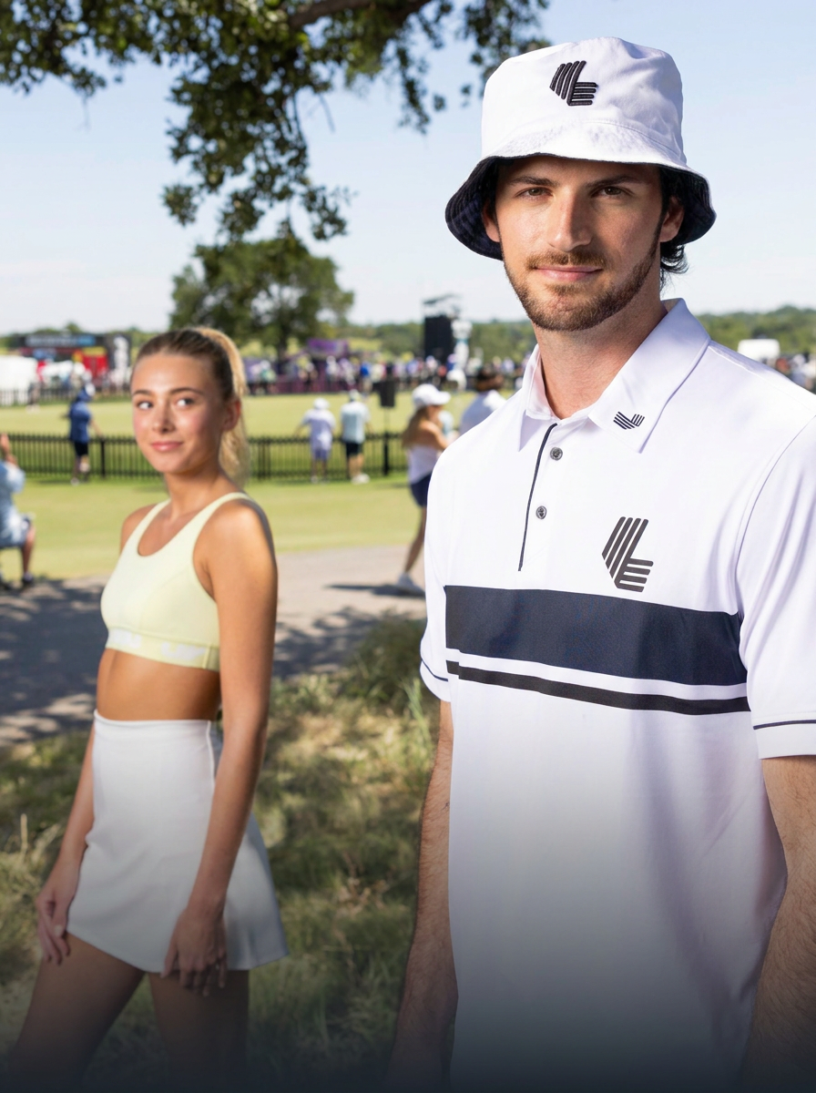 Two young adults, a man and a woman, standing outdoors at a golf event on a sunny day. The man wears a white bucket hat and a white polo shirt with black stripes and logos. The woman wears a yellow sports crop top and a white skirt. In the background, there are people, a grassy field, trees, and fencing.