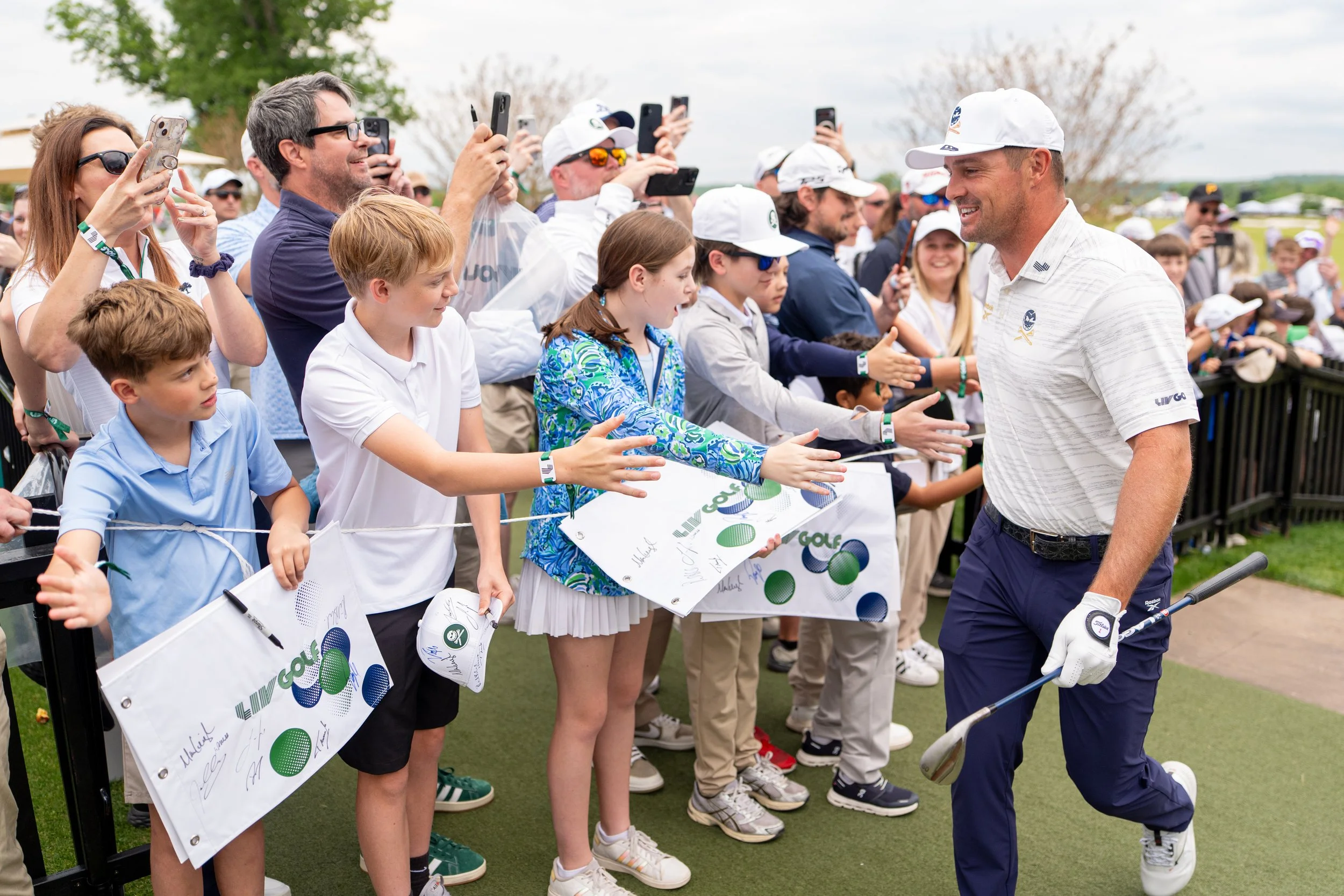 A group of children and adults at a golf tournament, with children signing autographs and a man in golf attire smiling and interacting with them.