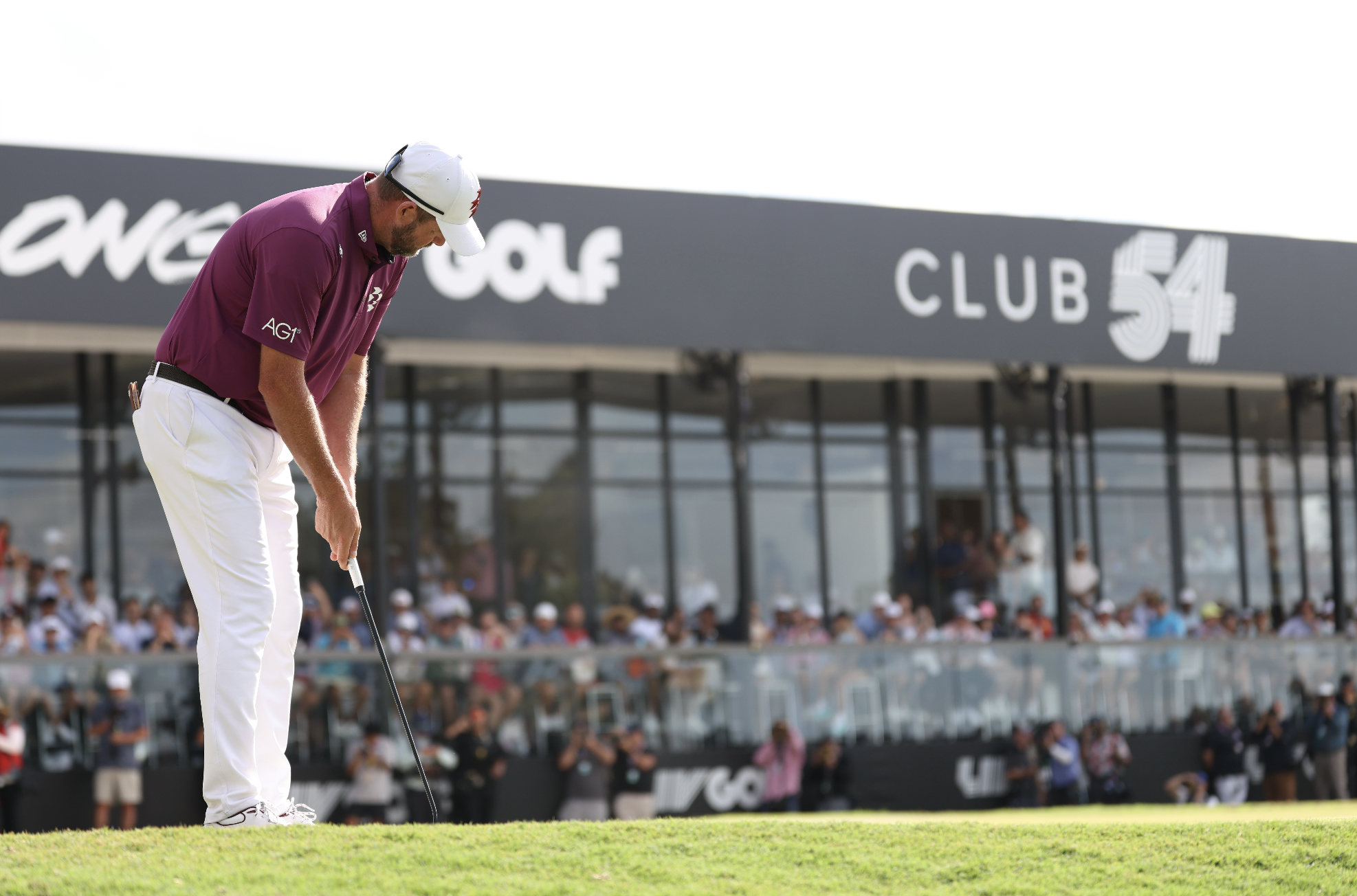 A man playing golf on a golf course with a crowd and a large sign in the background that reads "CLUB 54".
