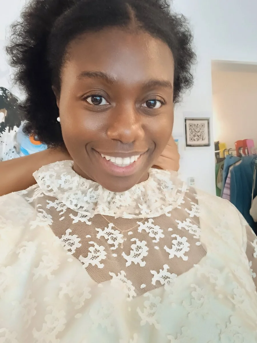 A woman smiling, wearing a white lace top with floral patterns and a ruffled collar.