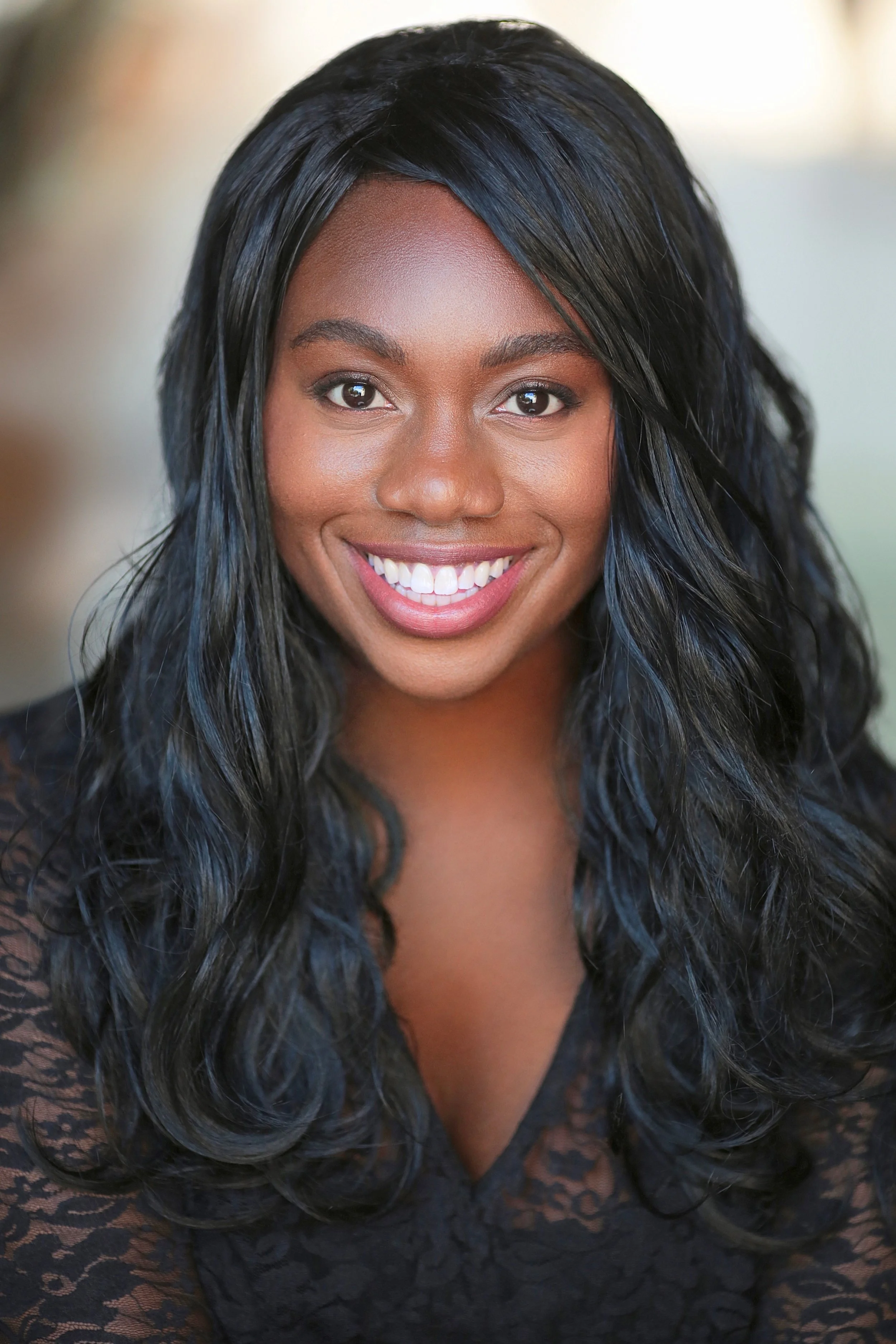 Close-up of a woman with dark, wavy hair, smiling, wearing a black lace top.