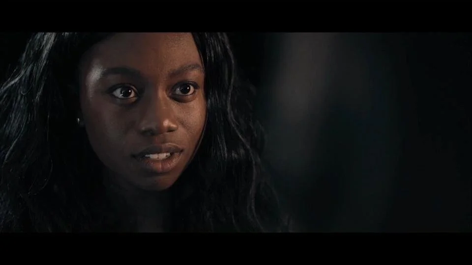 A woman with dark hair and expressive eyes looking slightly to the side in a dimly lit environment.