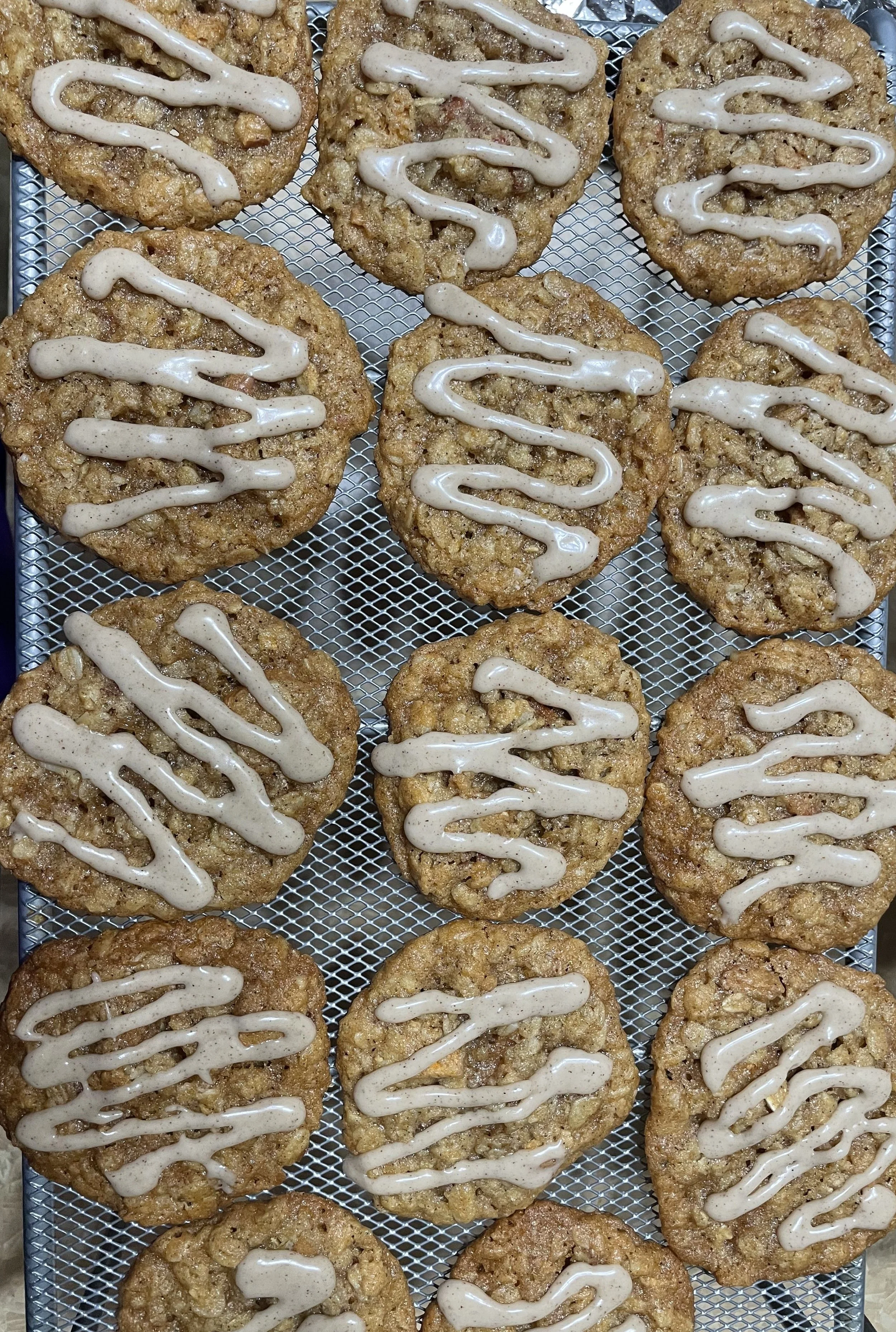 Oatmeal cookies with icing drizzle on a cooling rack.