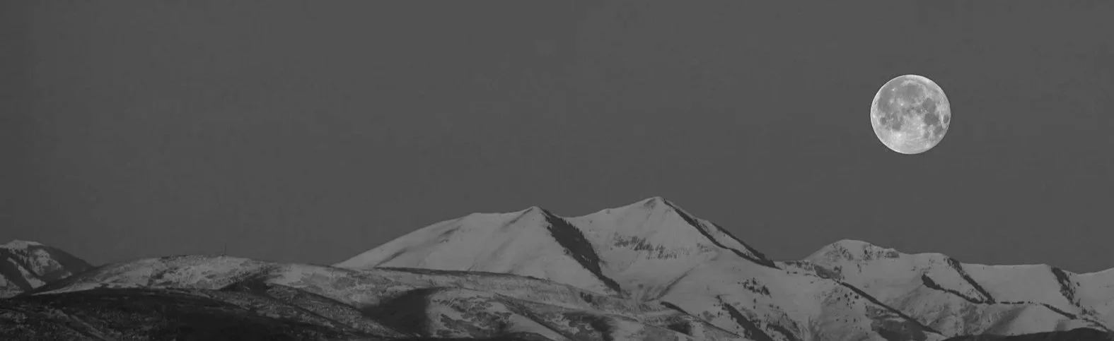 Snow-covered mountain range at night with a full moon in the sky.