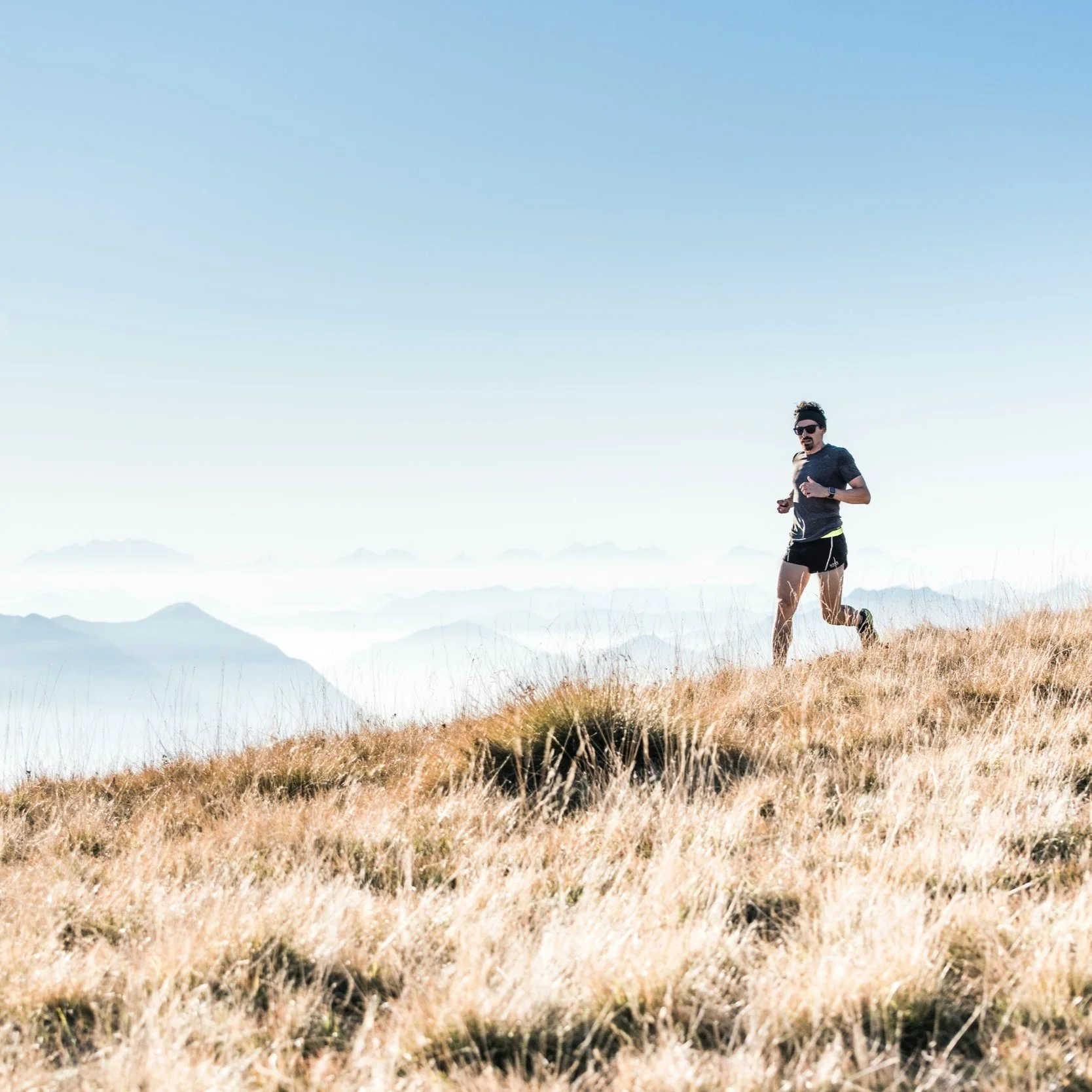 Person running on a grassy hill with mountains in the background under a clear blue sky.