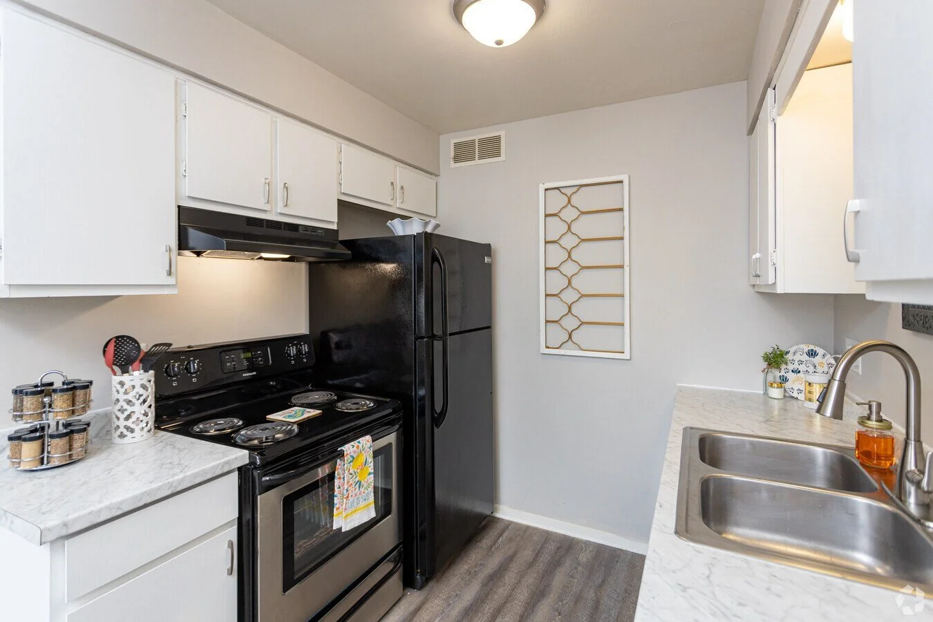 Kitchen with white cabinets, black appliances, a marble countertop, and a grayish-brown wood floor.