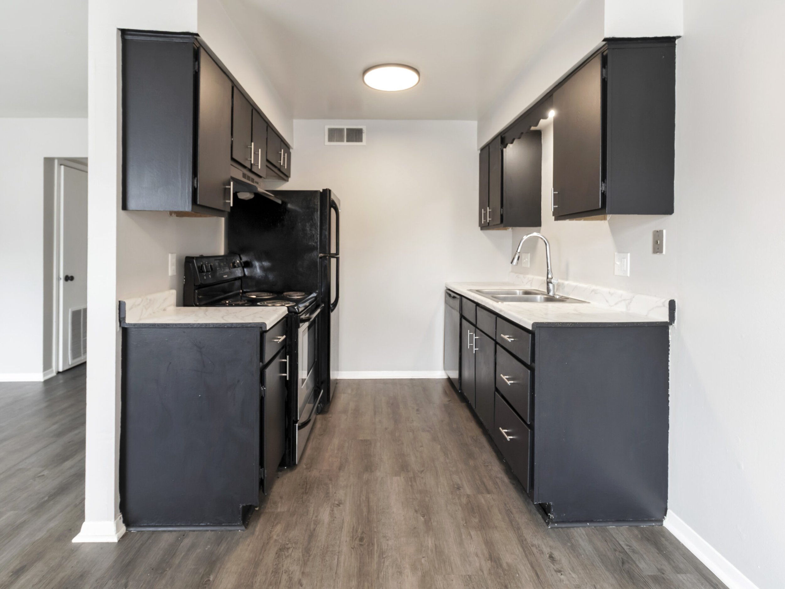 Kitchen with dark cabinets, white marble countertops, black appliances, and wood flooring.