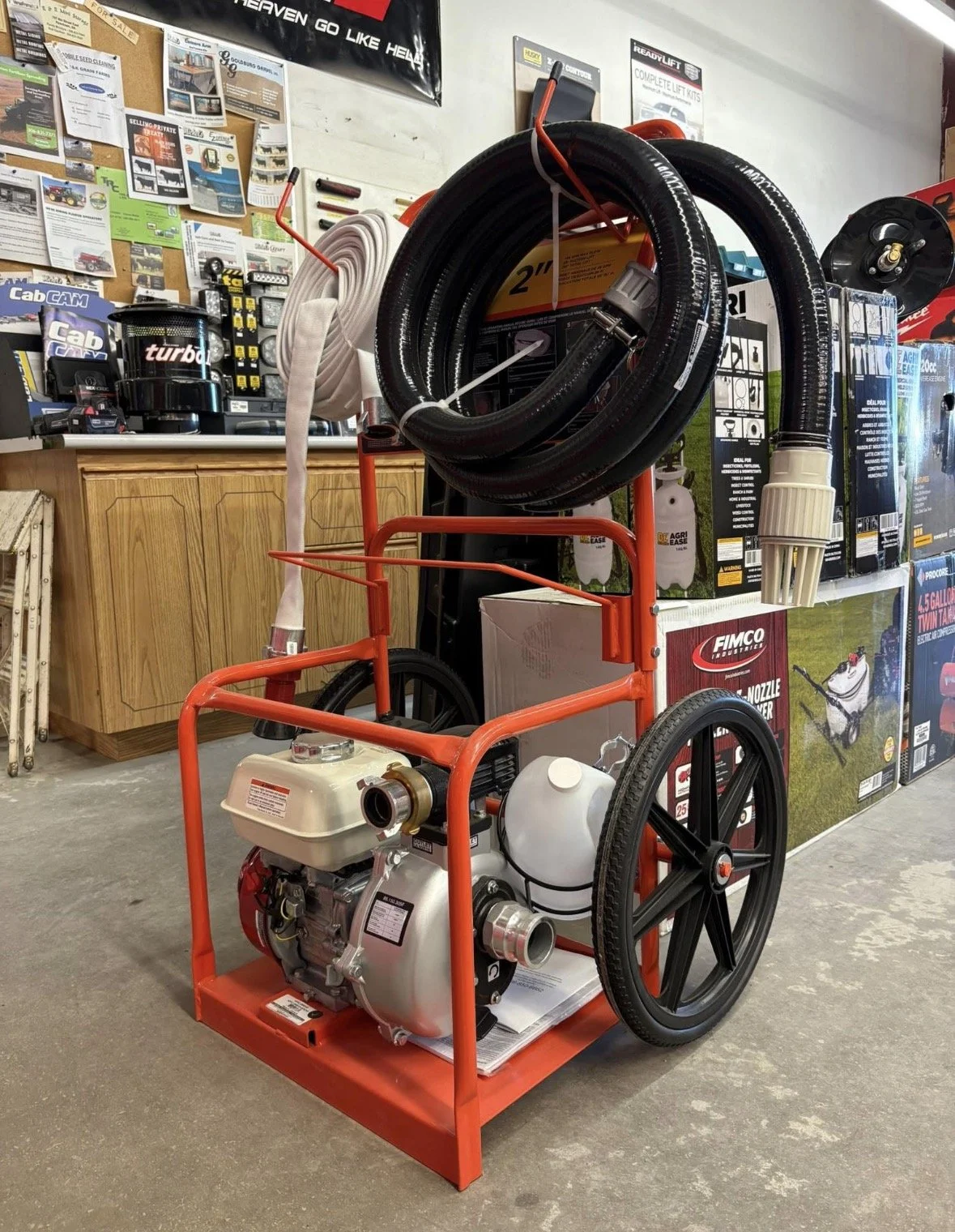 A portable water pump with a hose and a white filter, in a store display, with various tools and equipment in the background.