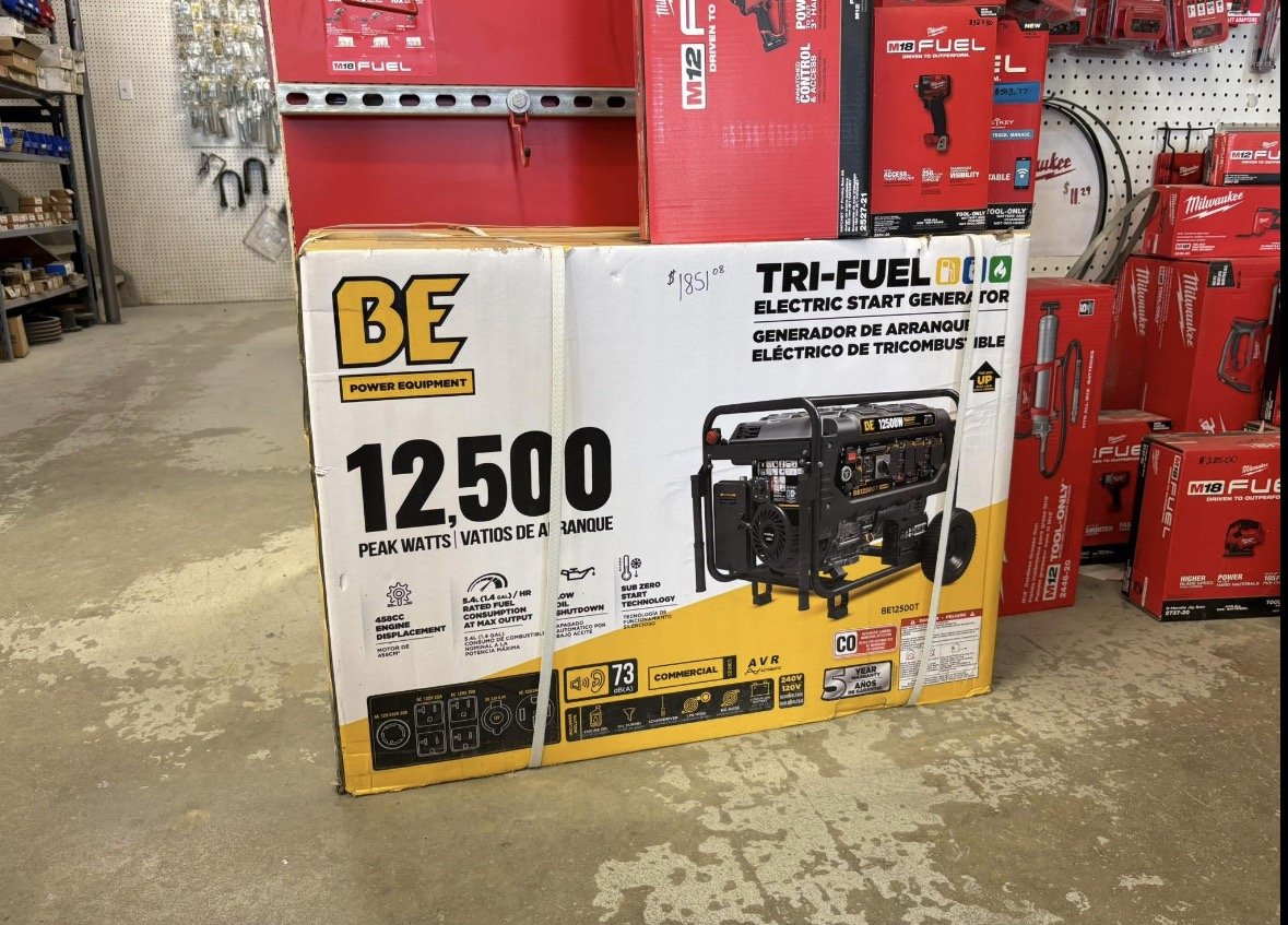 Box for BE power equipment, a TRI-FUEL electric start generator with 12,500 peak watts, displayed on a store floor with other power tools visible in the background.