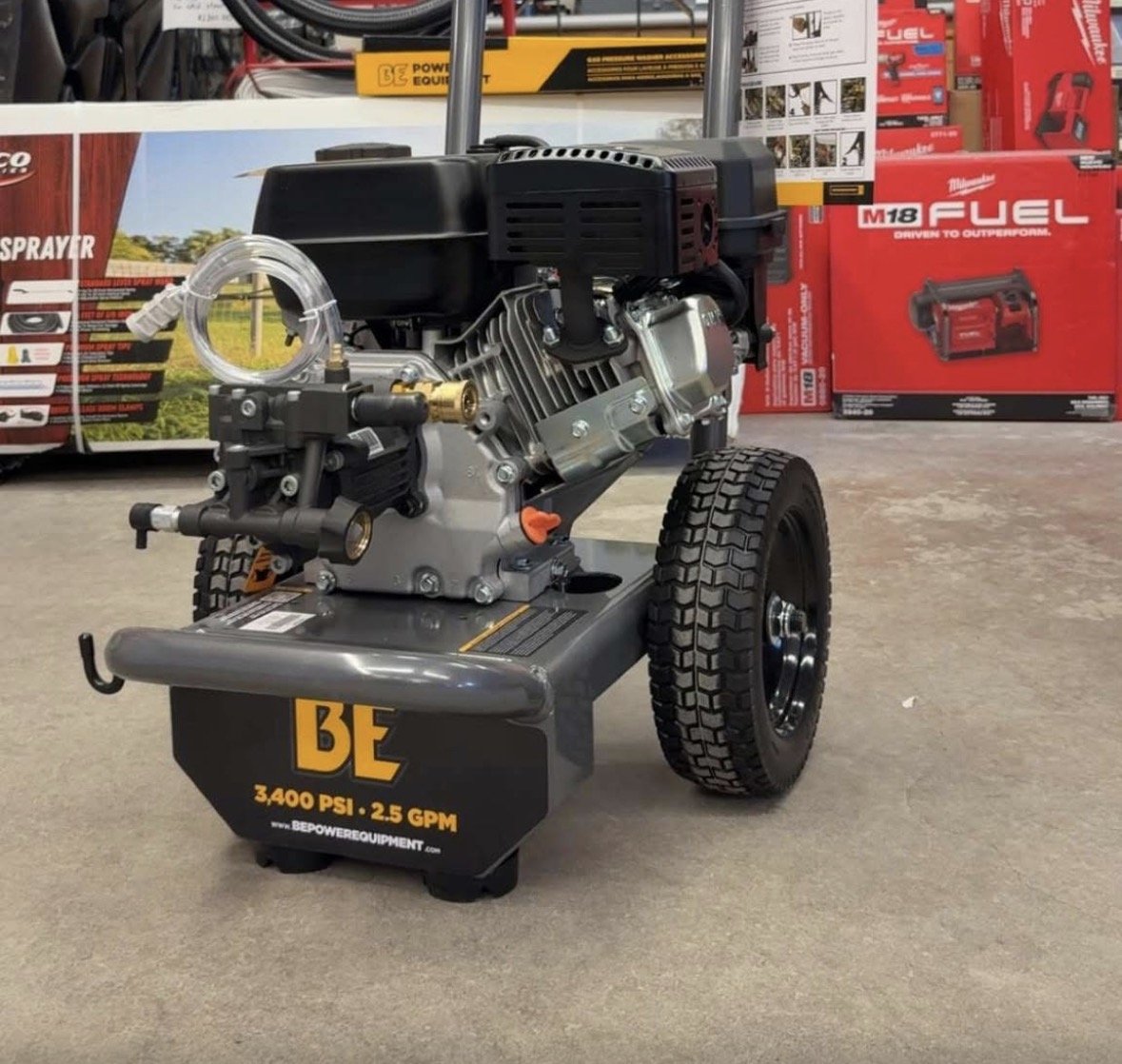 A portable air compressor with a black engine, silver components, and large black wheels, displayed in a retail store with power tool boxes in the background.
