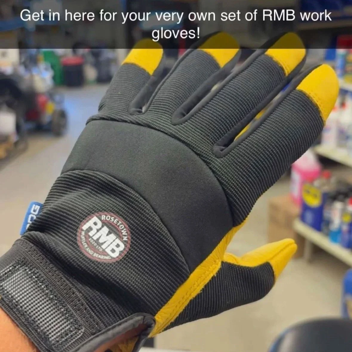 A worker's glove with a black and yellow design, featuring a logo that reads 'RMB Rosetown Workwear and Bearing,' displayed in a hardware store aisle.