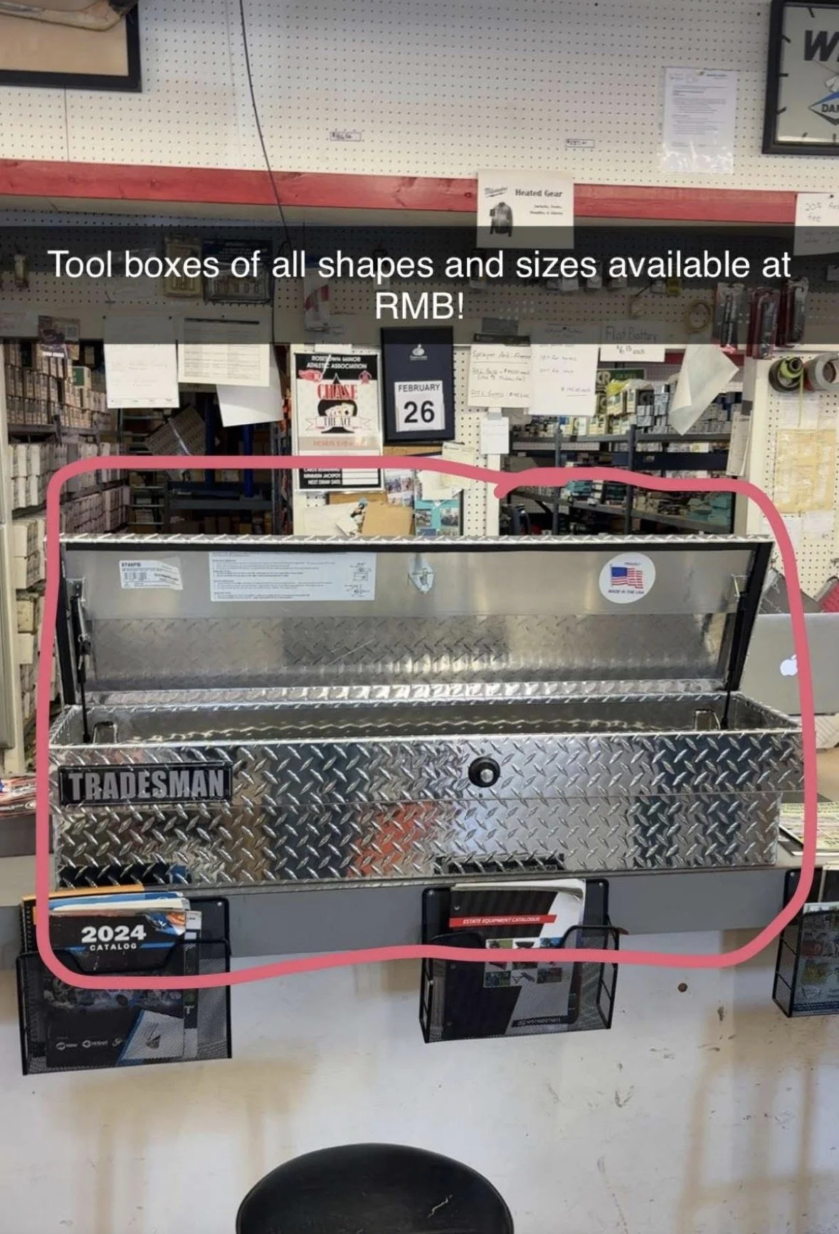 A display of a empty silver tool box with a black lock in a hardware store, surrounded by various tool advertisements and product displays, with a sign that reads 'Tool boxes of all shapes and sizes available at RMB!'