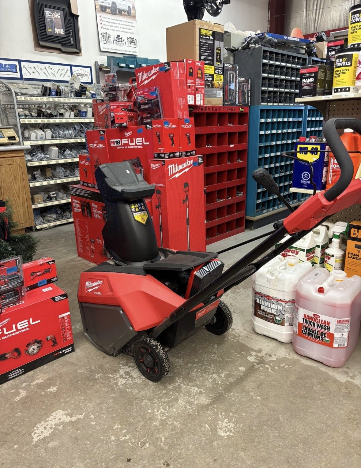 A red leaf blower in an aisle of a hardware store, surrounded by various tools, boxes, and cleaning supplies.