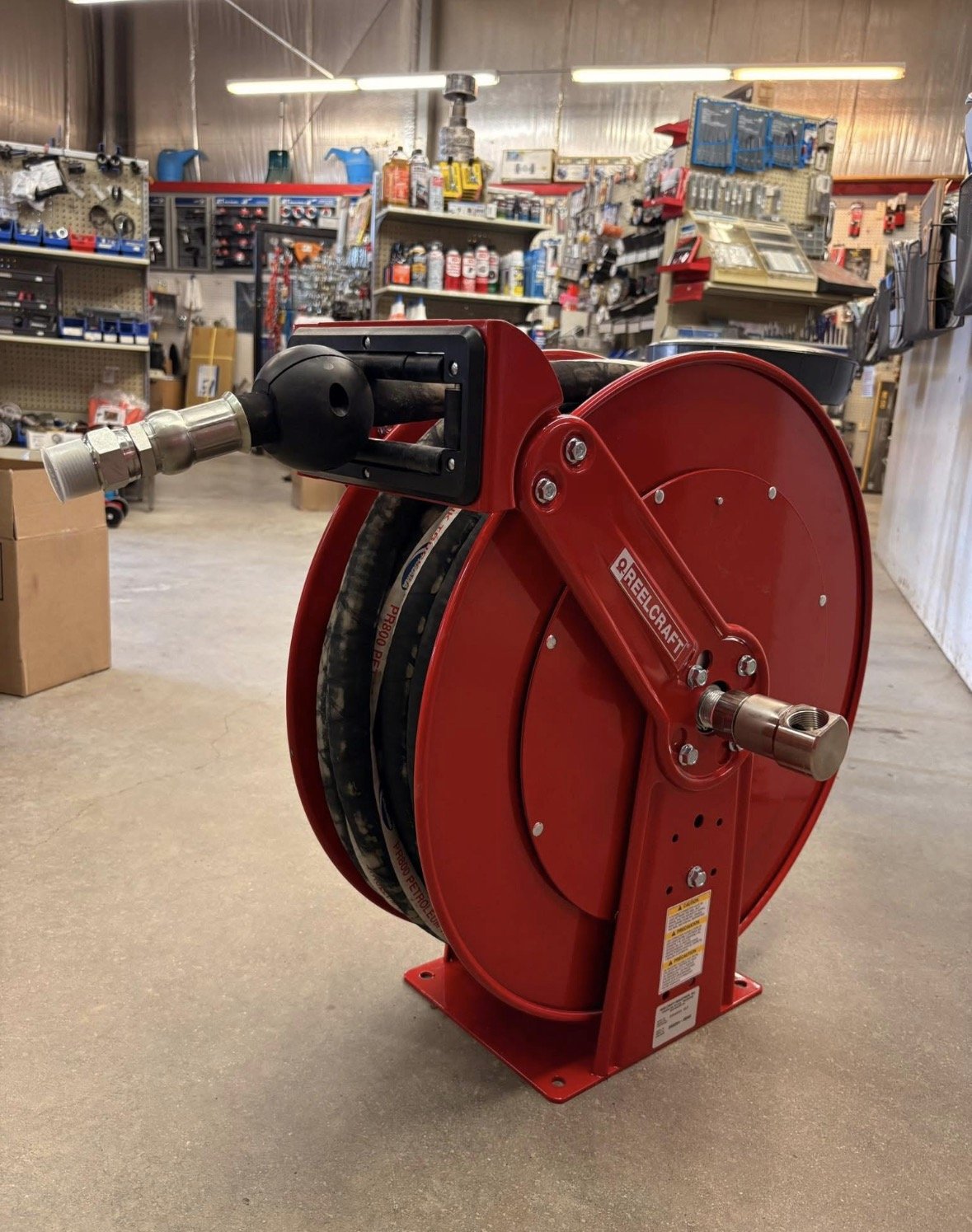A red fire hose reel with a black connector in a hardware store aisle, surrounded by shelves with various tools and supplies.