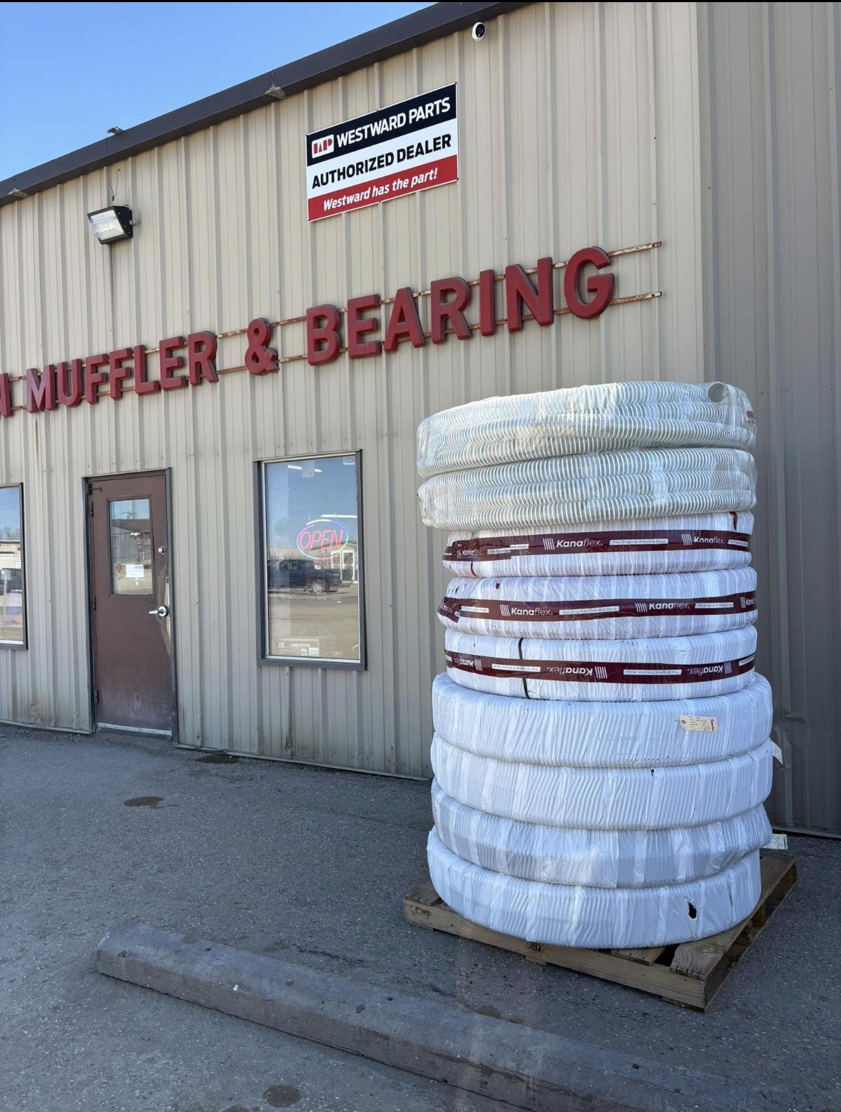 Outside of a building with a sign for muffler and bearing parts, featuring a large stack of mattress springs or coils on a wooden pallet.