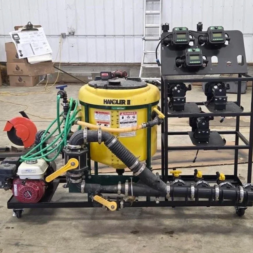 An industrial water pump system with hoses, a yellow holder tank, gauges, and control panels, set in a workshop or warehouse.