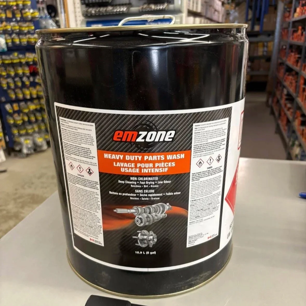 A large black container of EMZone heavy-duty parts wash sitting on a white surface in a store aisle.