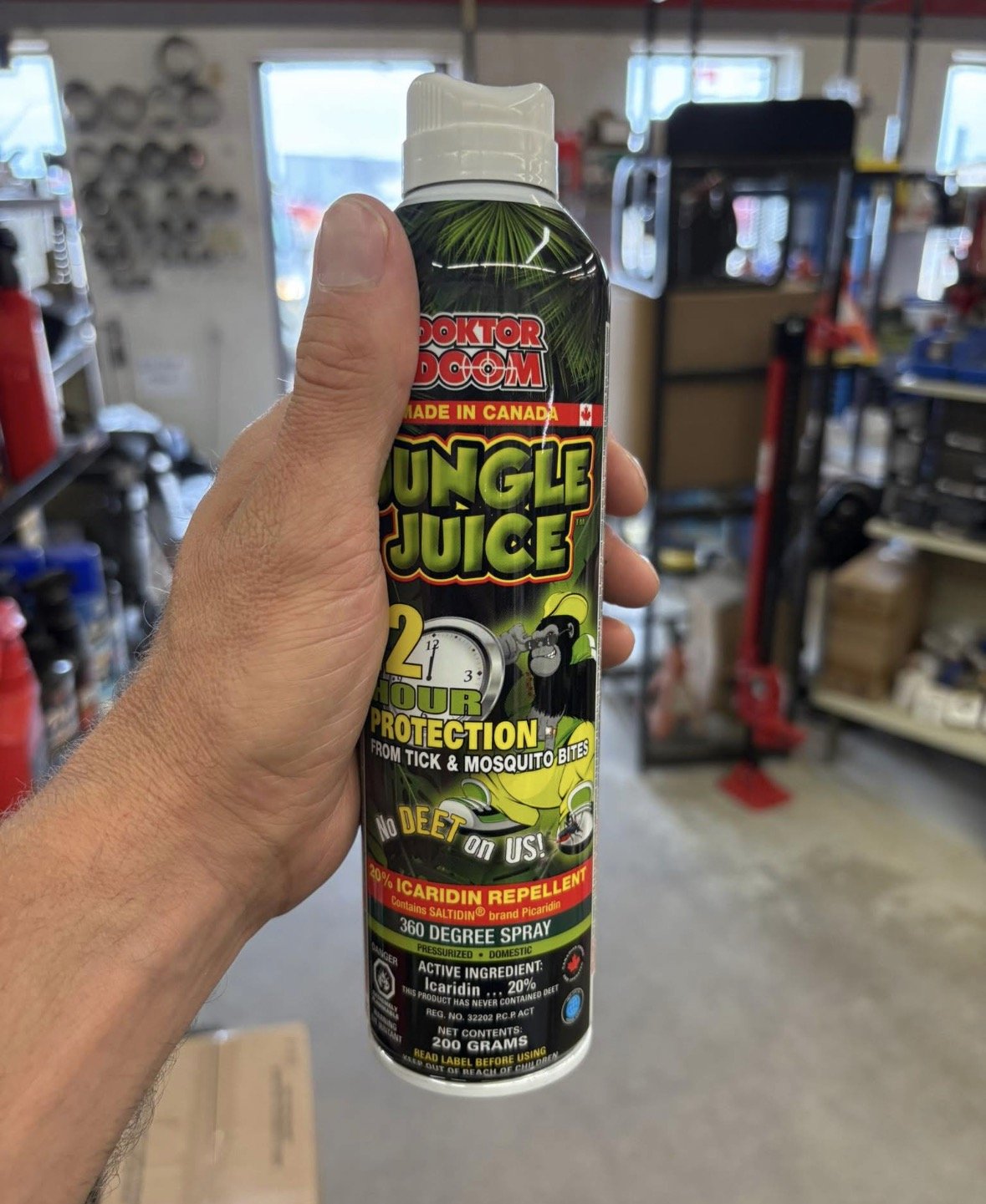 Hand holding a can of Jungle Juice insect spray in a hardware store. The spray is for protection from ticks and mosquitoes, contains Icaridin, and has a 360-degree spray nozzle.