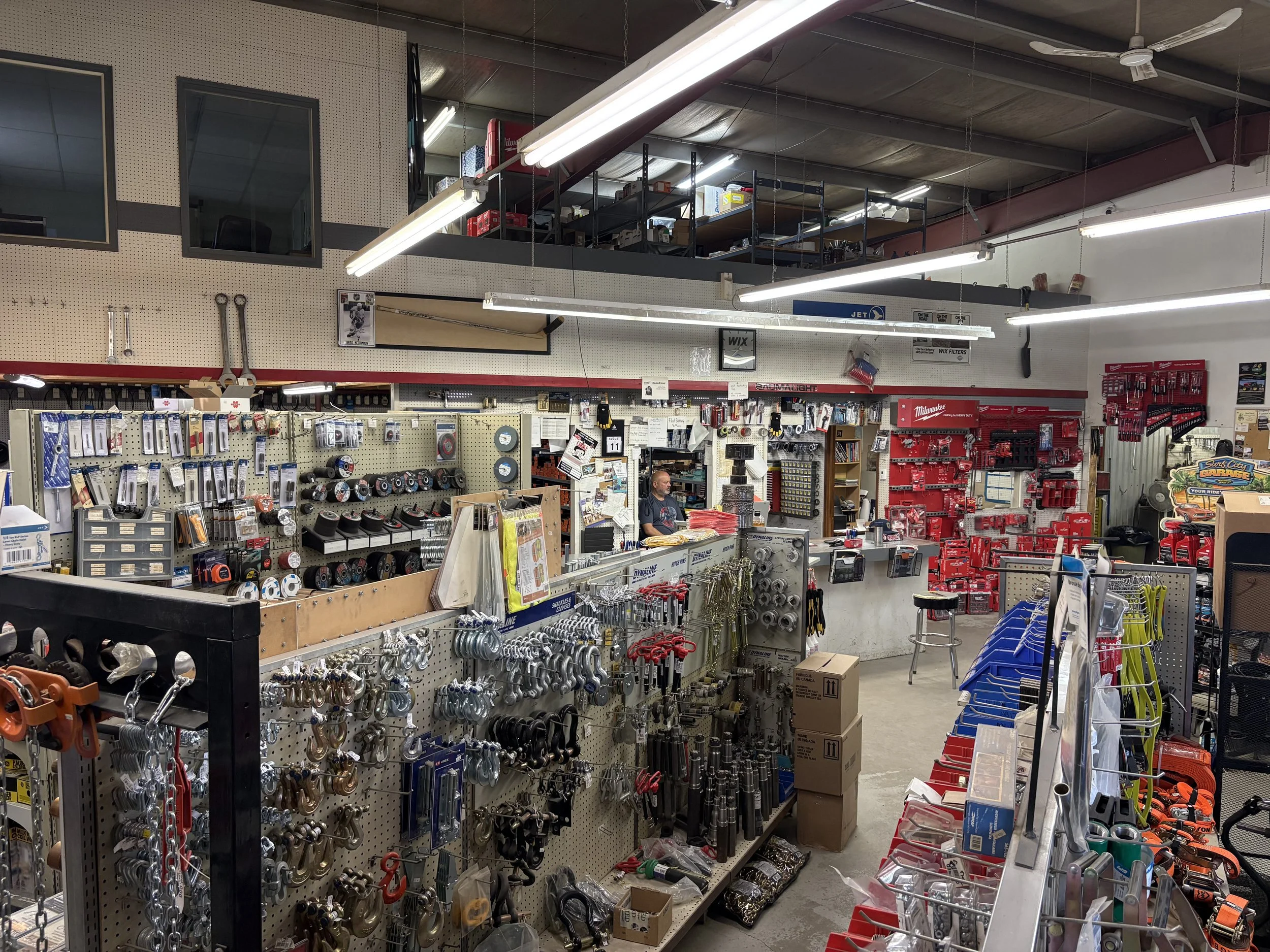 The image shows the interior of a hardware store with various tools, equipment, and supplies organized on shelves and display racks.
