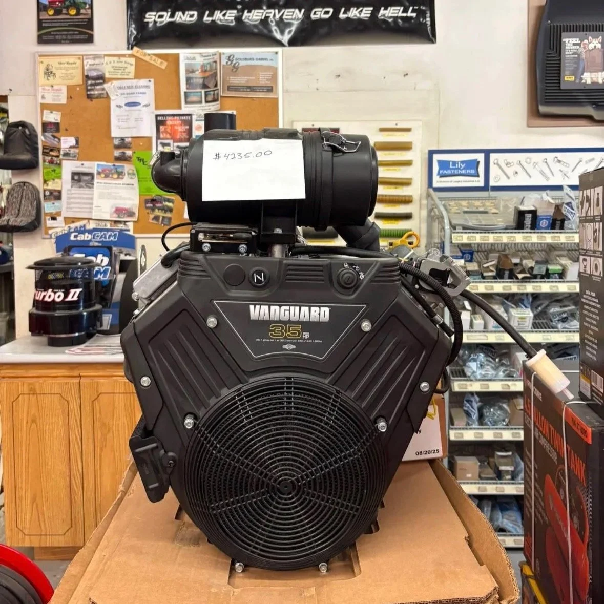 Black Vanguard 35 HP engine with a note showing $4235.00 price. It is placed on a cardboard box inside a store filled with various automotive parts and tools.
