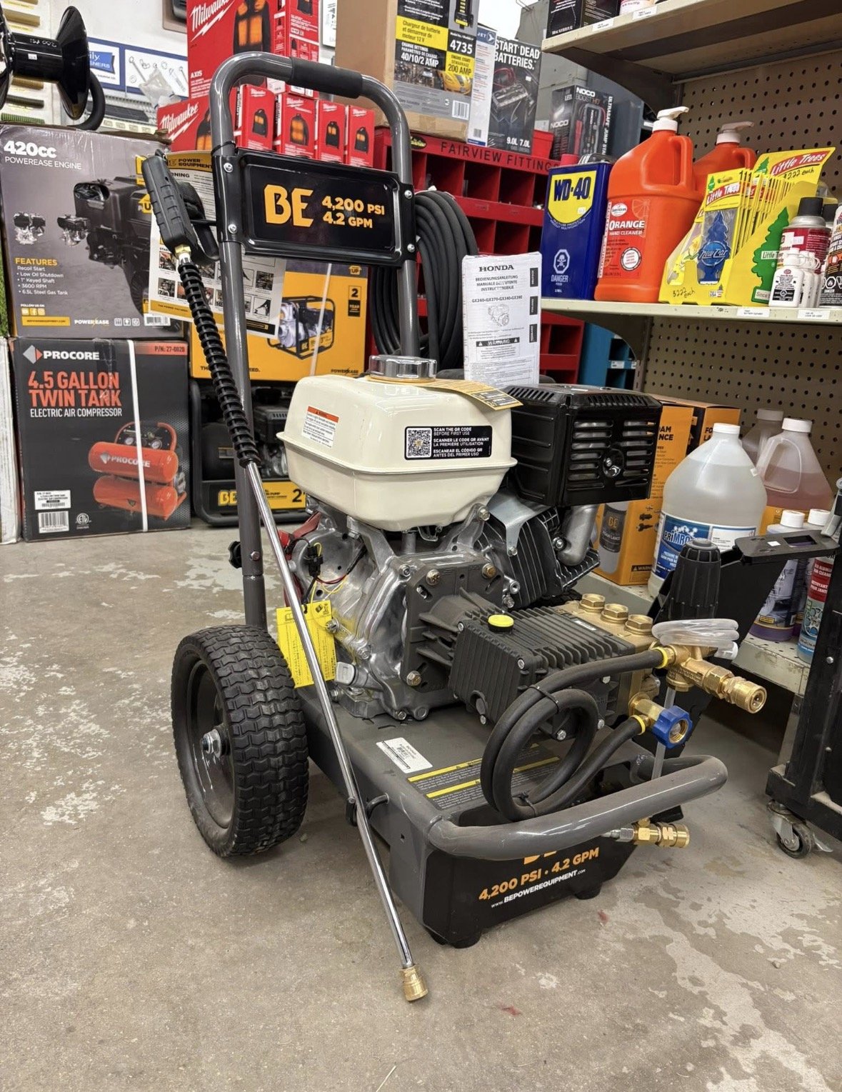 A portable air compressor on the floor of a hardware store, with shelves of various tools and supplies in the background.