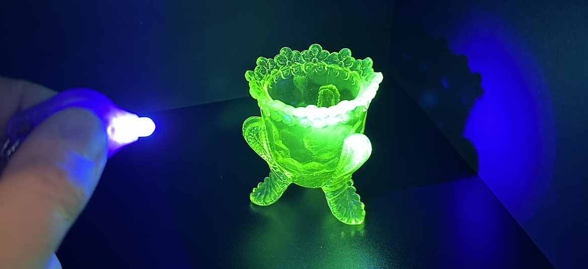 Glowing green turtle-shaped object with a bowl on its back, held under ultraviolet light in a dark room.