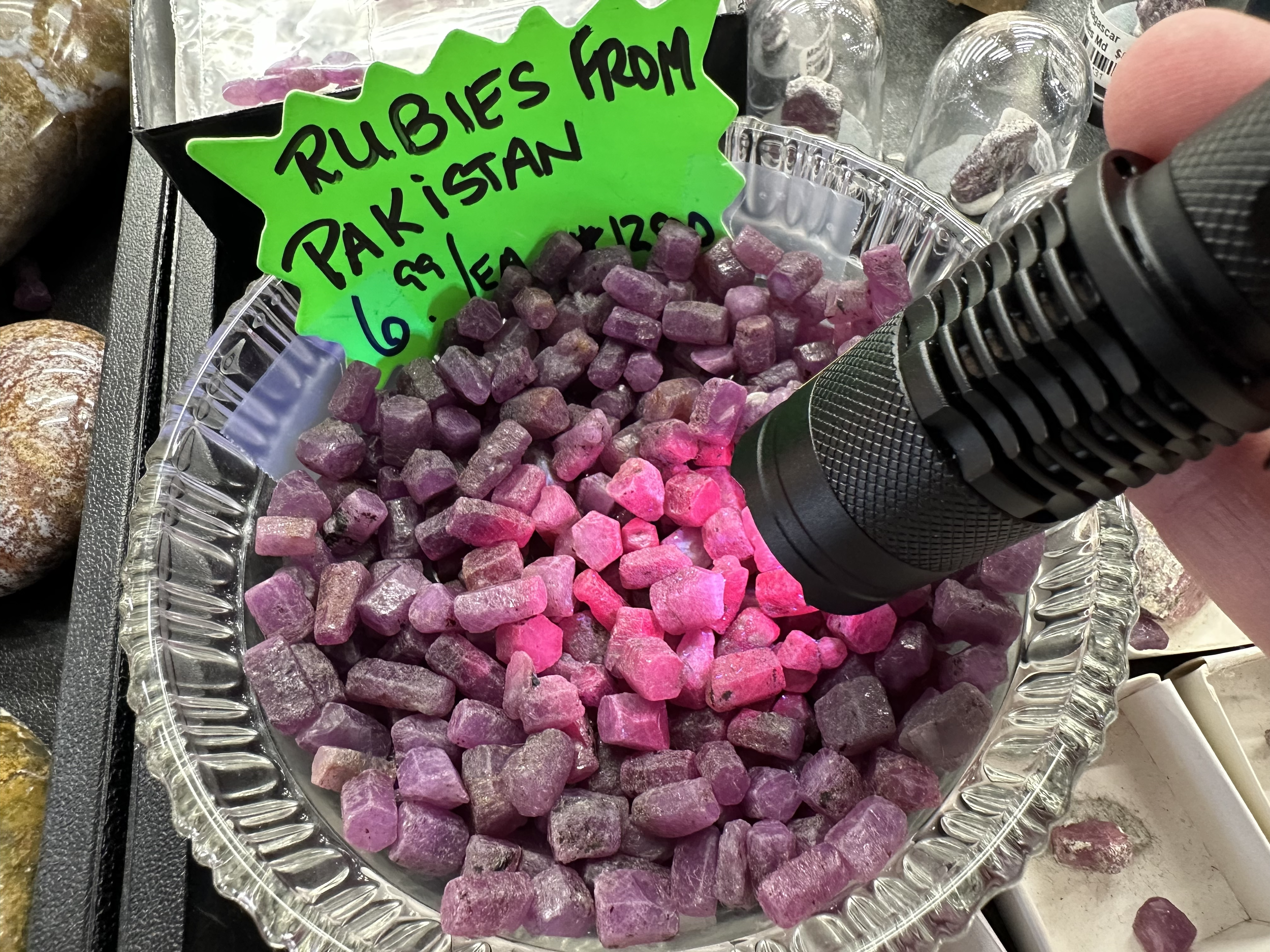 A tray of pink and purple Rubies from Pakistan with a green handwritten sign indicating their origin and price.