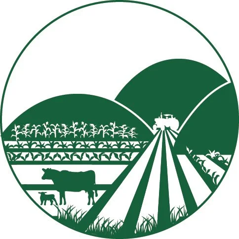 A circular logo featuring a landscape with farm fields, animals, and hills, with a tractor on a road.