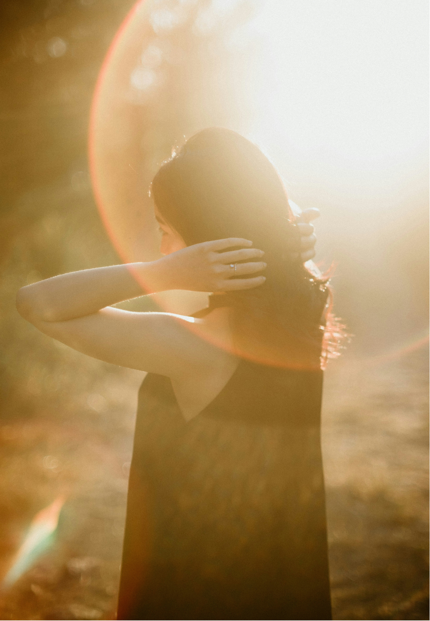 Person with wet hair embracing themselves, backlit by a bright, warm sunlight, creating a lens flare effect.