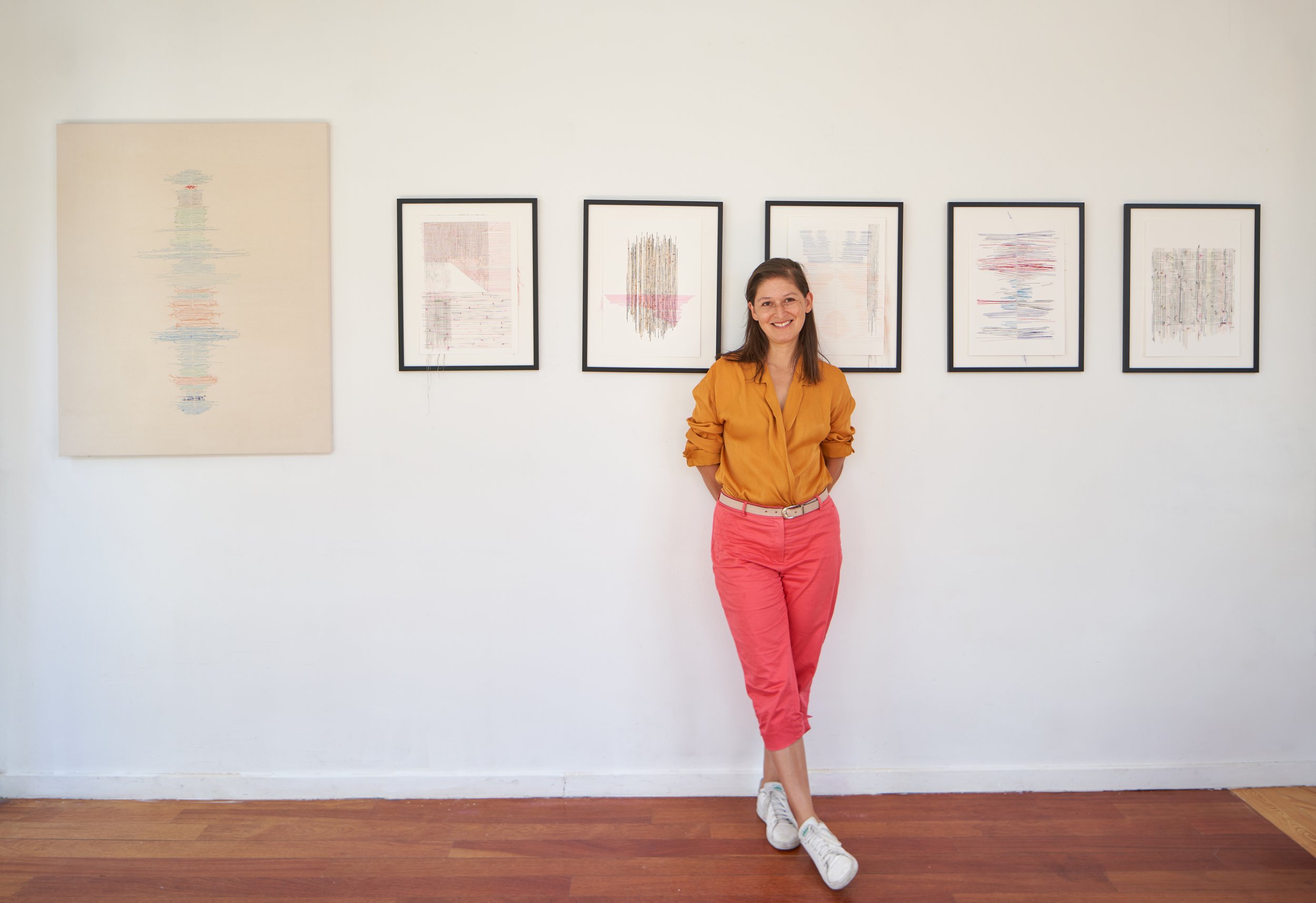 Mujer sonriendo de pie en una galería de arte con cuadros abstractos en la pared.