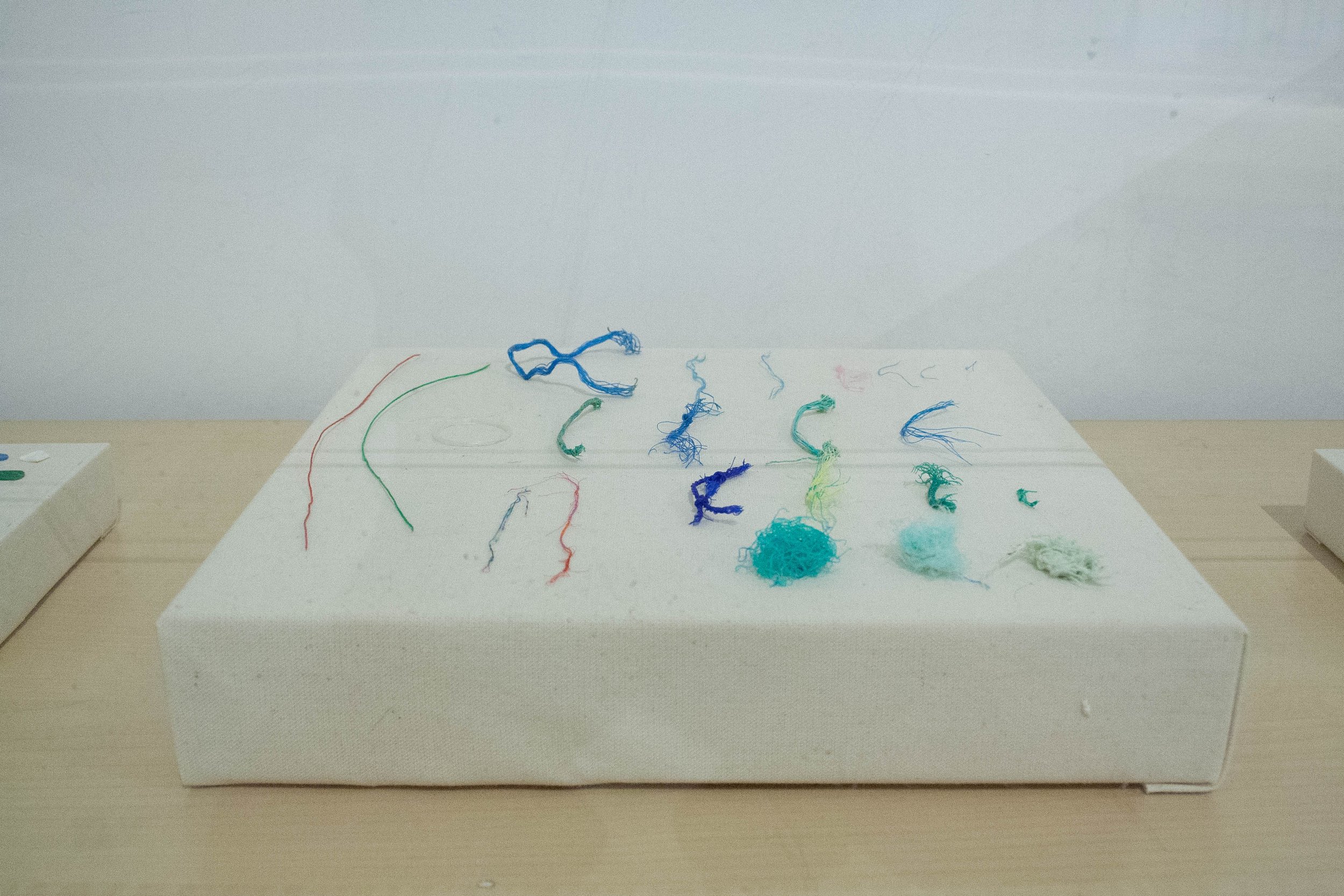 Diverse hilos de colores en una superficie blanca sobre una mesa de madera, con elementos de fibrocitos de colores y ovillos de hilo, en un entorno de trabajo o arte.