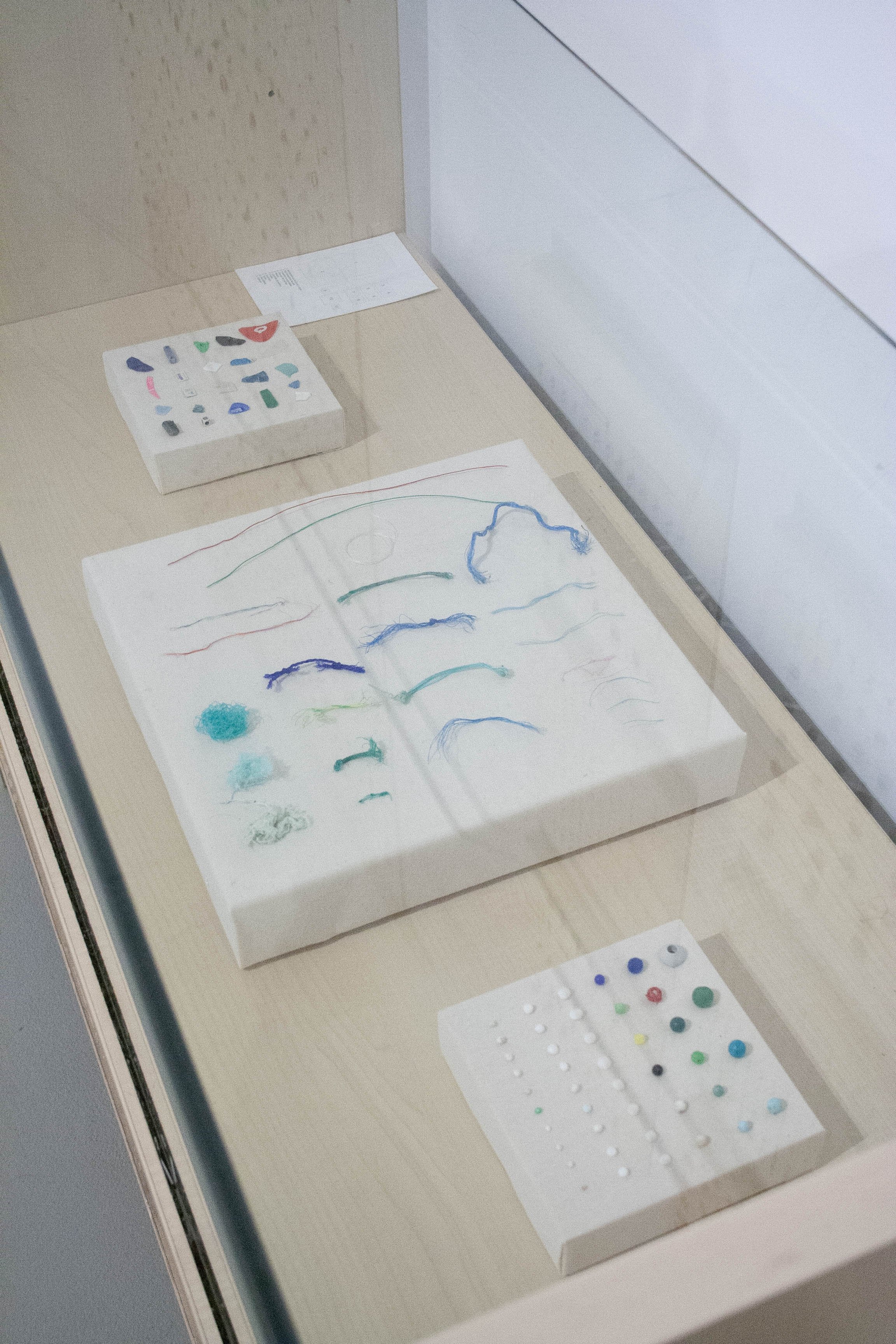 Dibujo en papel con líneas en diferentes colores, pequeños objetos de plástico de varios colores, y algunas piezas con patrones y formas en una caja y en la mesa.