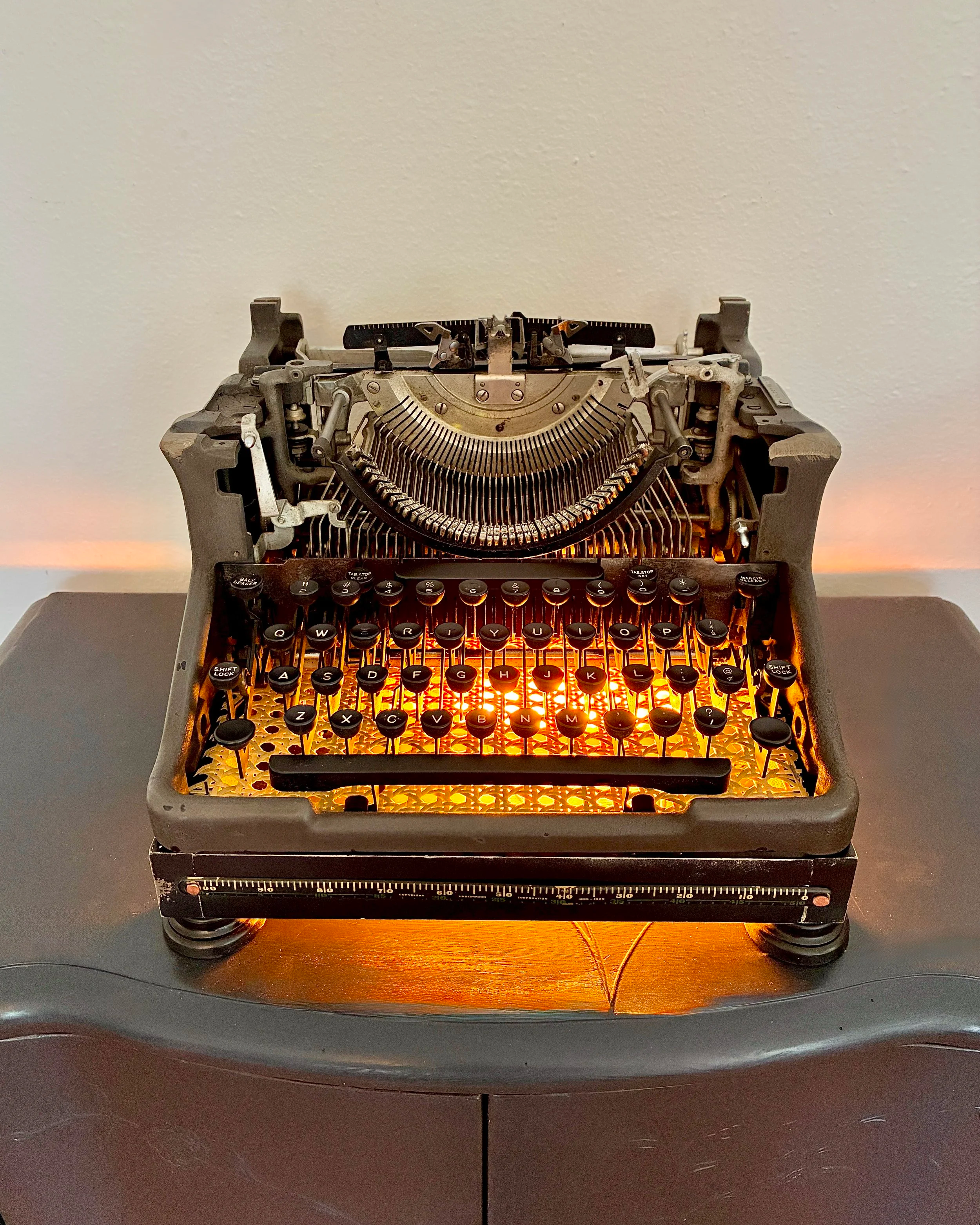 Close-up of vintage typewriter with backlit keys on a dark table against a light-colored wall.