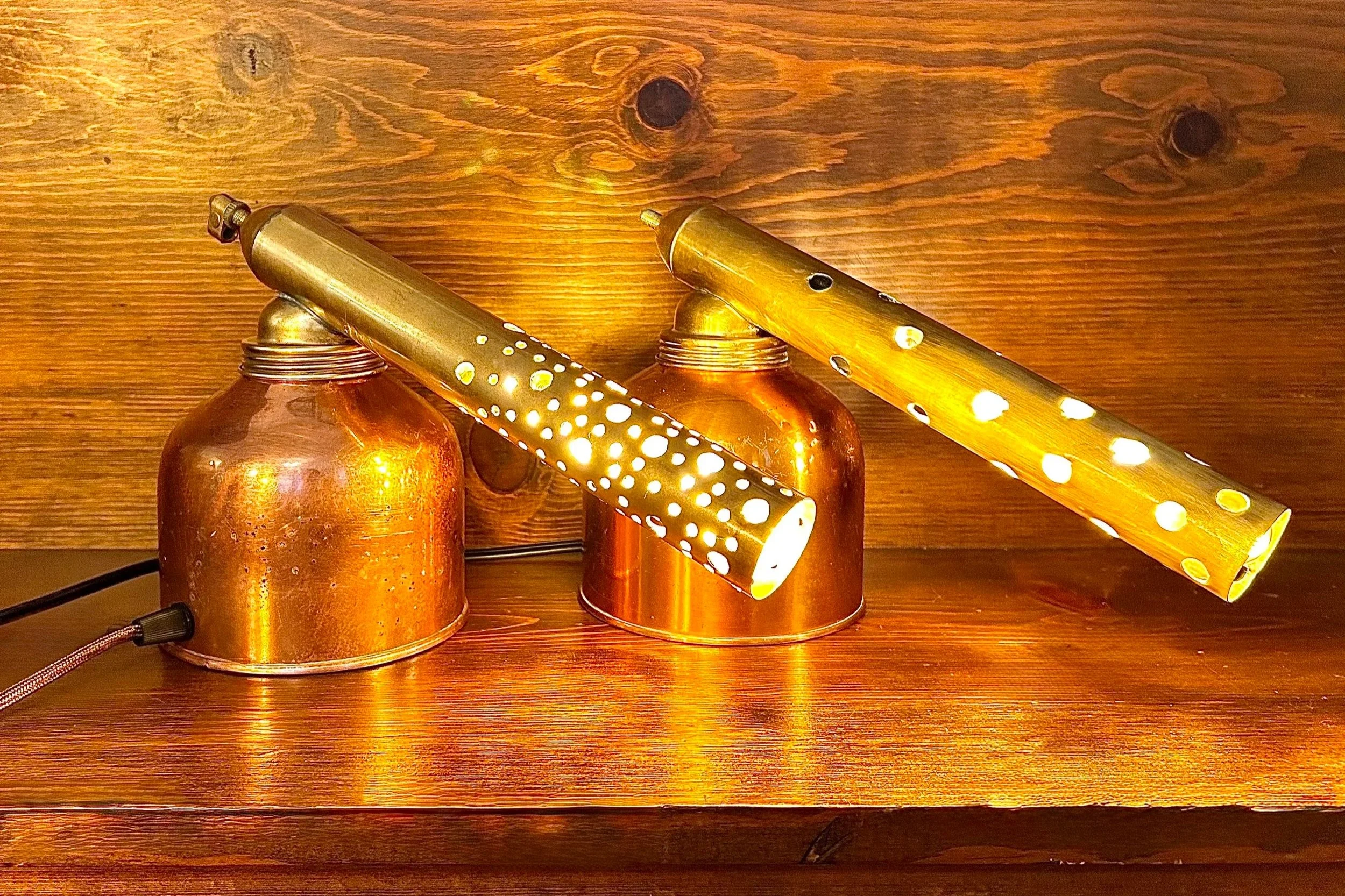 Two vintage-style table lamps with perforated shade holders resting on a wooden surface against a wooden wall.
