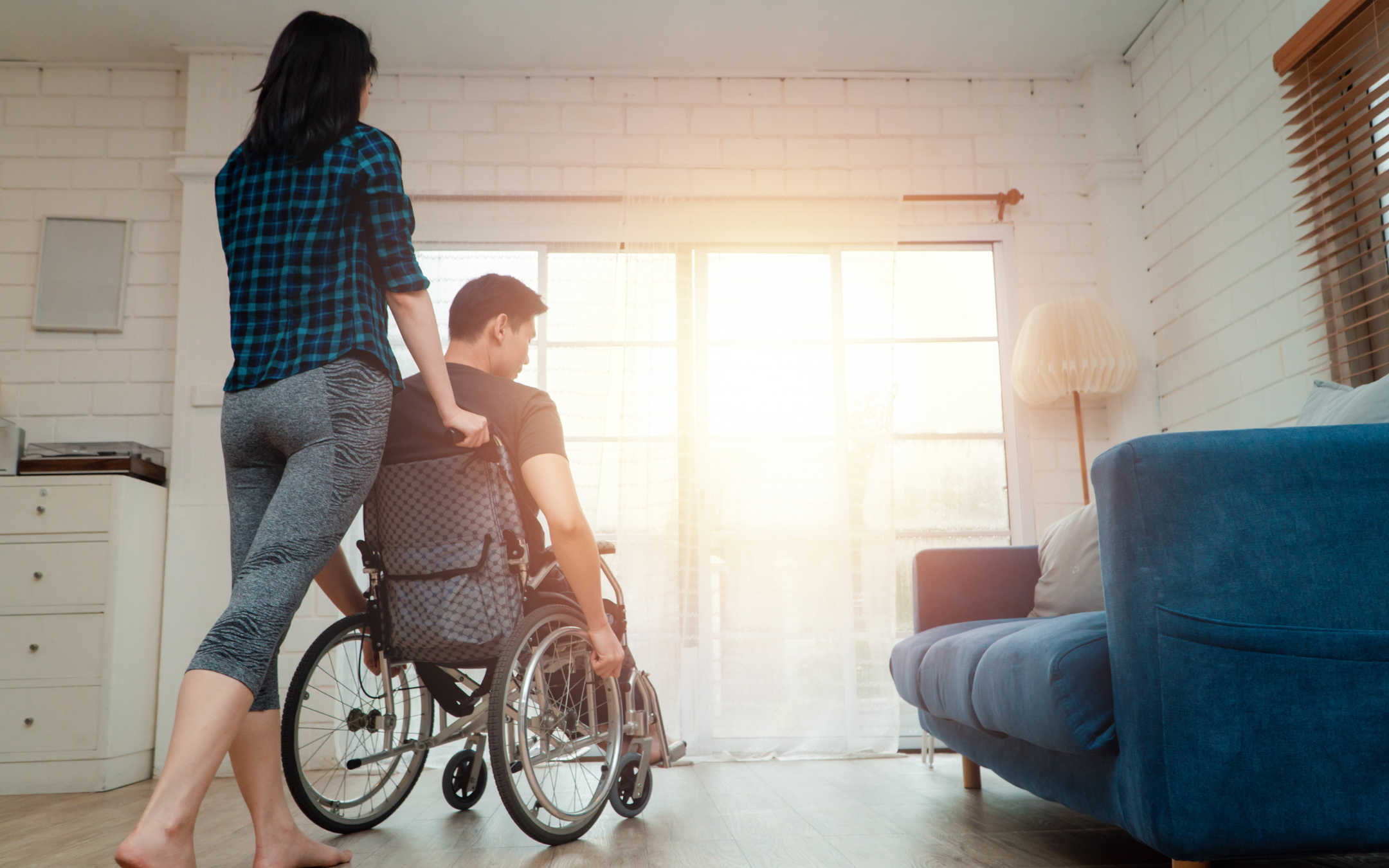 Caregiver assisting wheelchair user through open living room representing the improved home mobility and accessibility renovations provided by Melesh Construction Dallas serving the DFW Metroplex