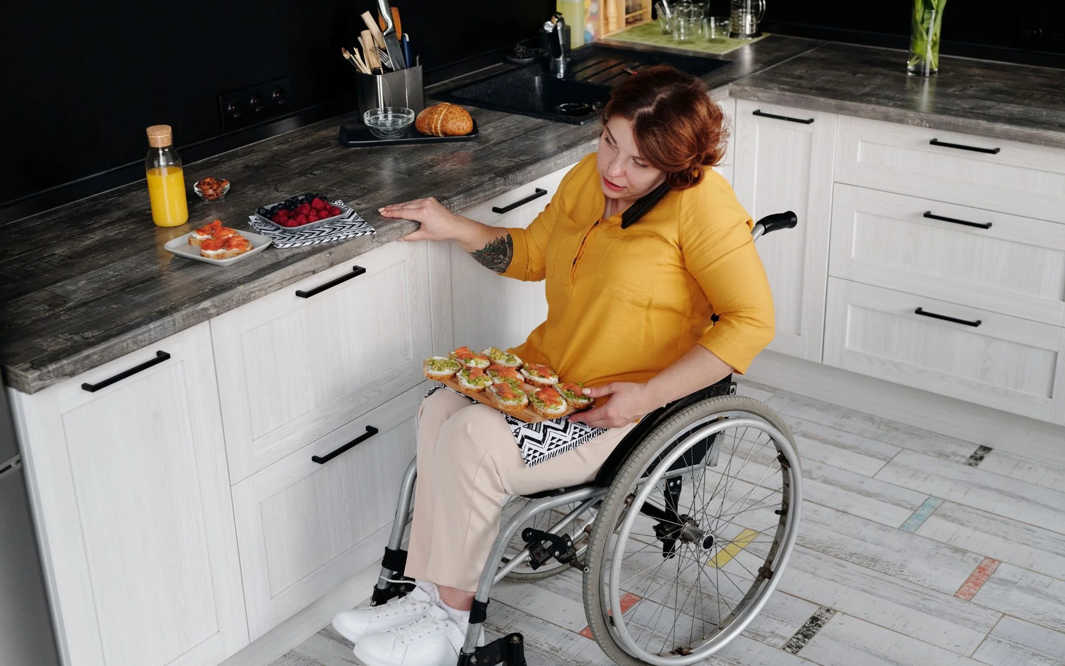 Woman in wheelchair independently using an accessible kitchen with lowered countertops and open floor clearance, representing mobility renovation work by Melesh Construction Dallas