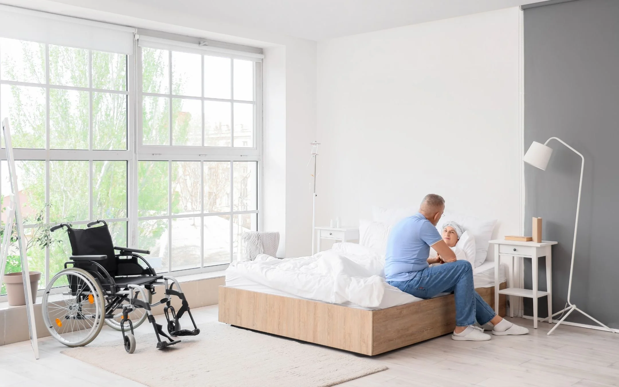 Caregiver assisting patient in accessible bedroom with wheelchair representing aging-in-place bedroom modification work by Melesh Construction Dallas serving the DFW Metroplex