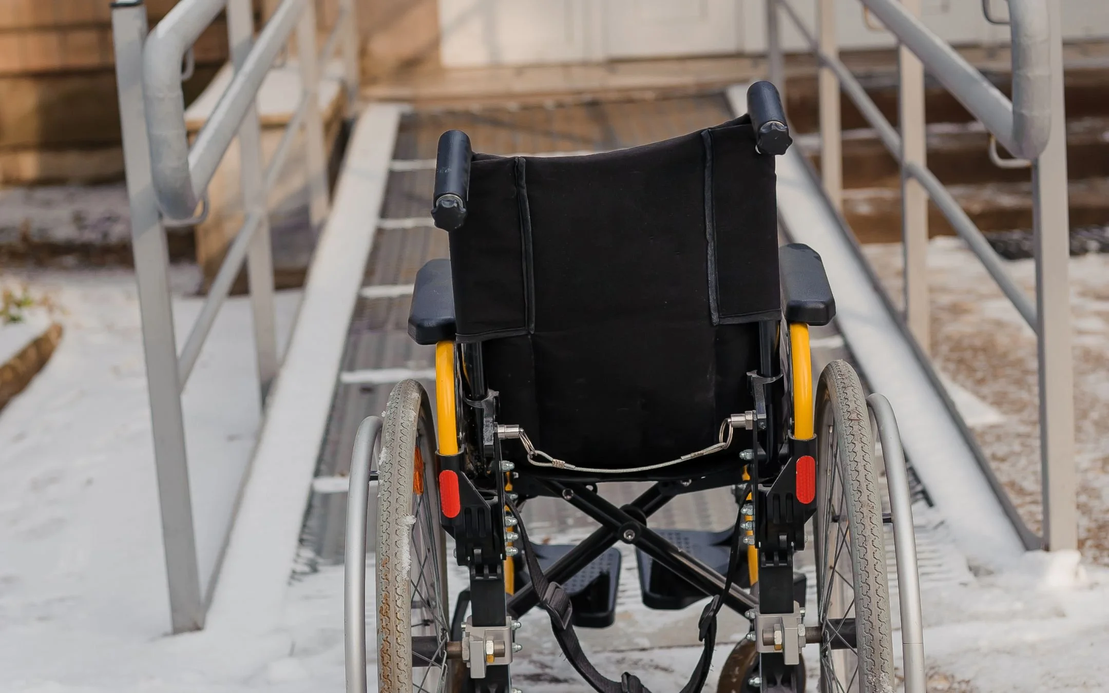 Wheelchair positioned at base of residential accessibility ramp with metal handrails installed by Melesh Construction Dallas for safe independent home entry