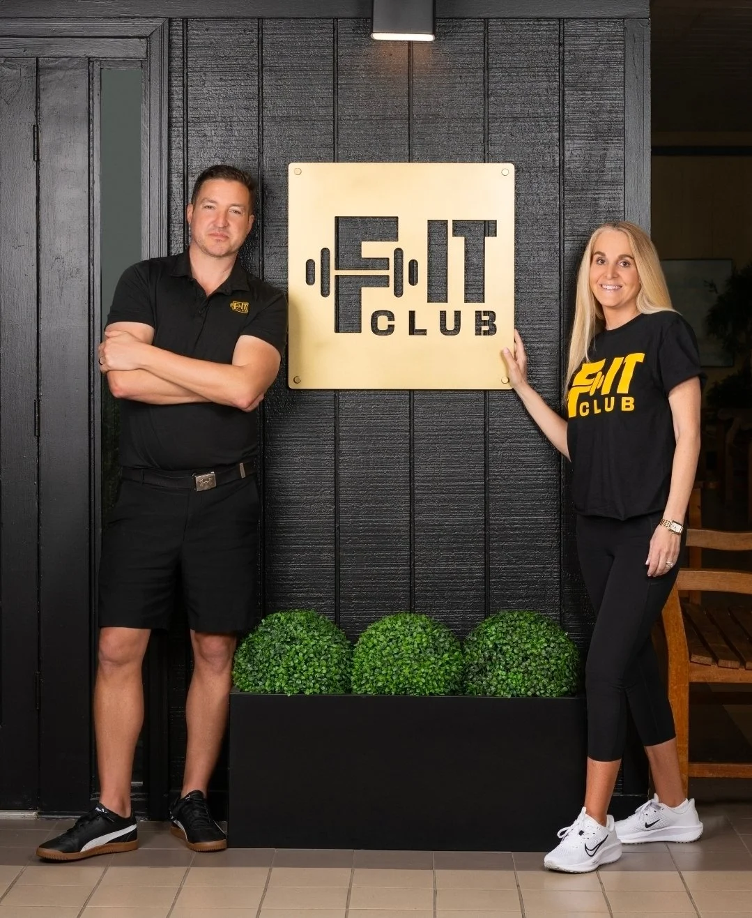 Man and woman standing beside a sign that reads 'FIT CLUB' at a fitness center.