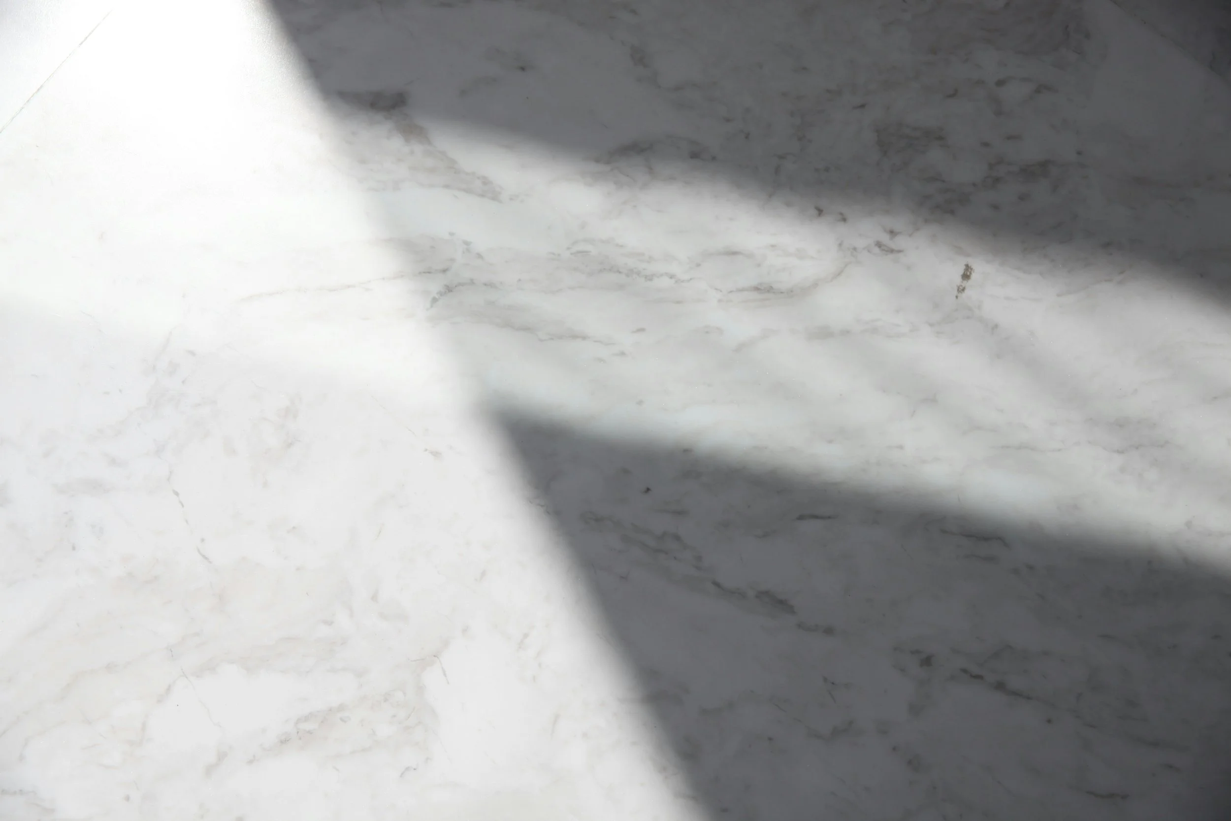 Close-up of a white marble surface with gray veining and a shadow cast across it.