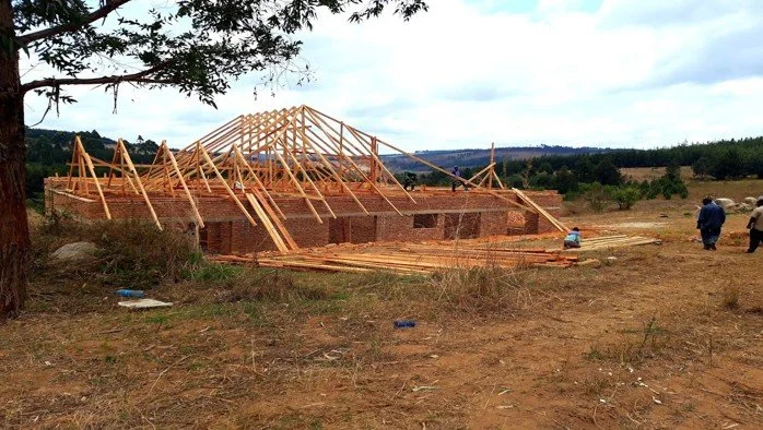 Wooden frame construction of a building on a rural construction site with people working, under a cloudy sky.
