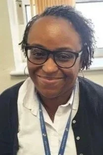 A woman wearing glasses and a white shirt with a dark cardigan, smiling in an indoor setting.