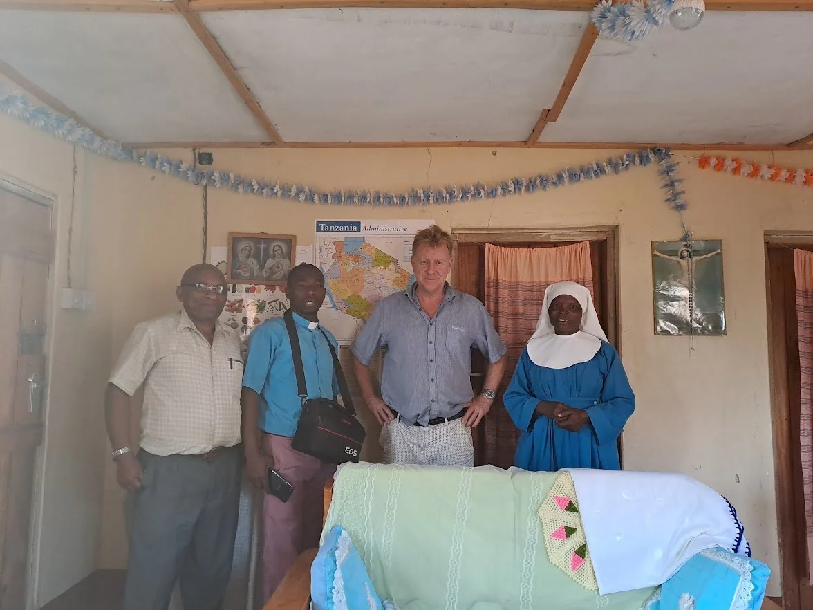 Four people standing inside a room decorated for a celebration with blue and orange streamers, a Bible, and a Tanzanian map.