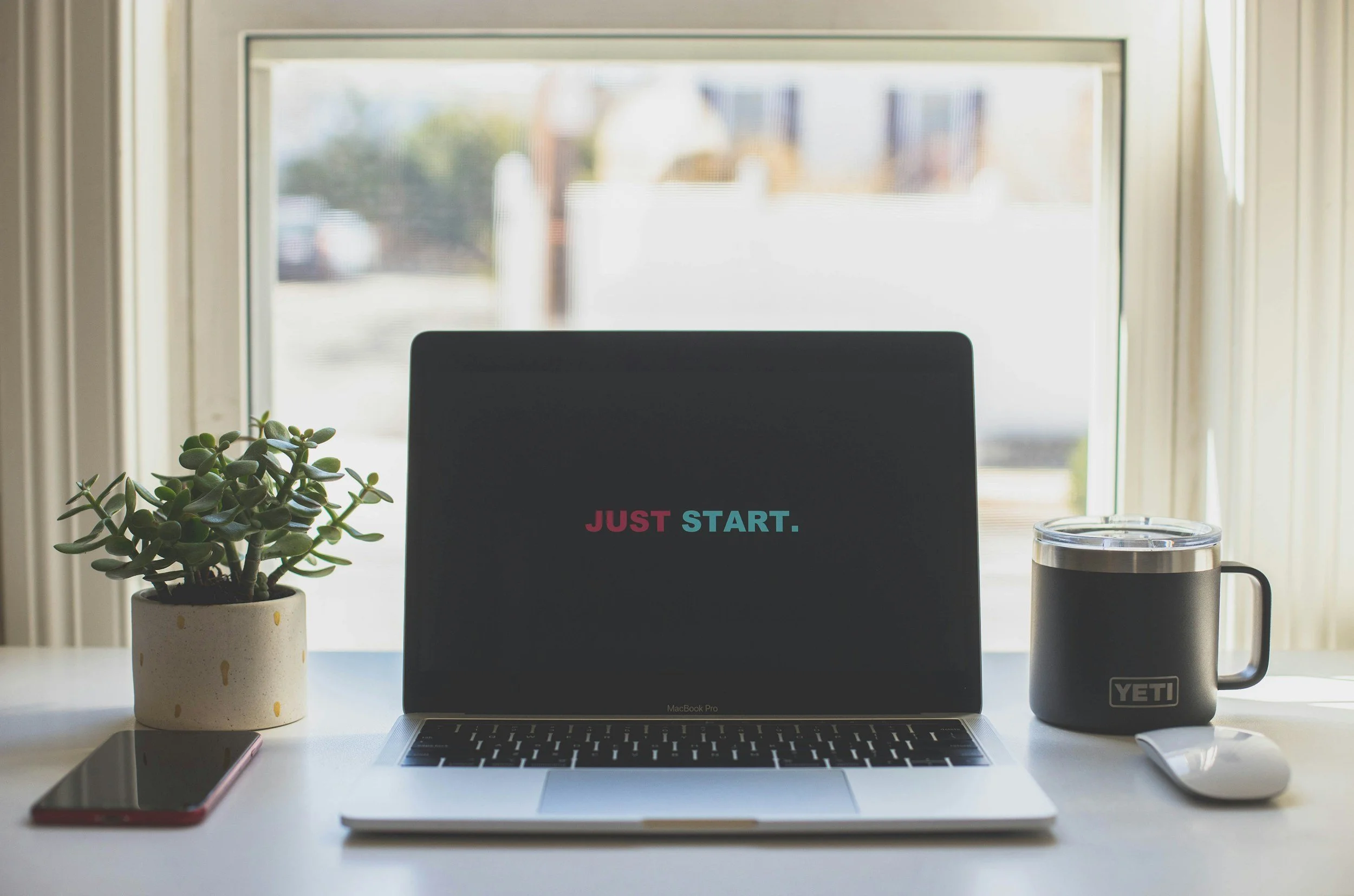 A laptop with a black screen and the words "Just. Start." in pink and blue text.