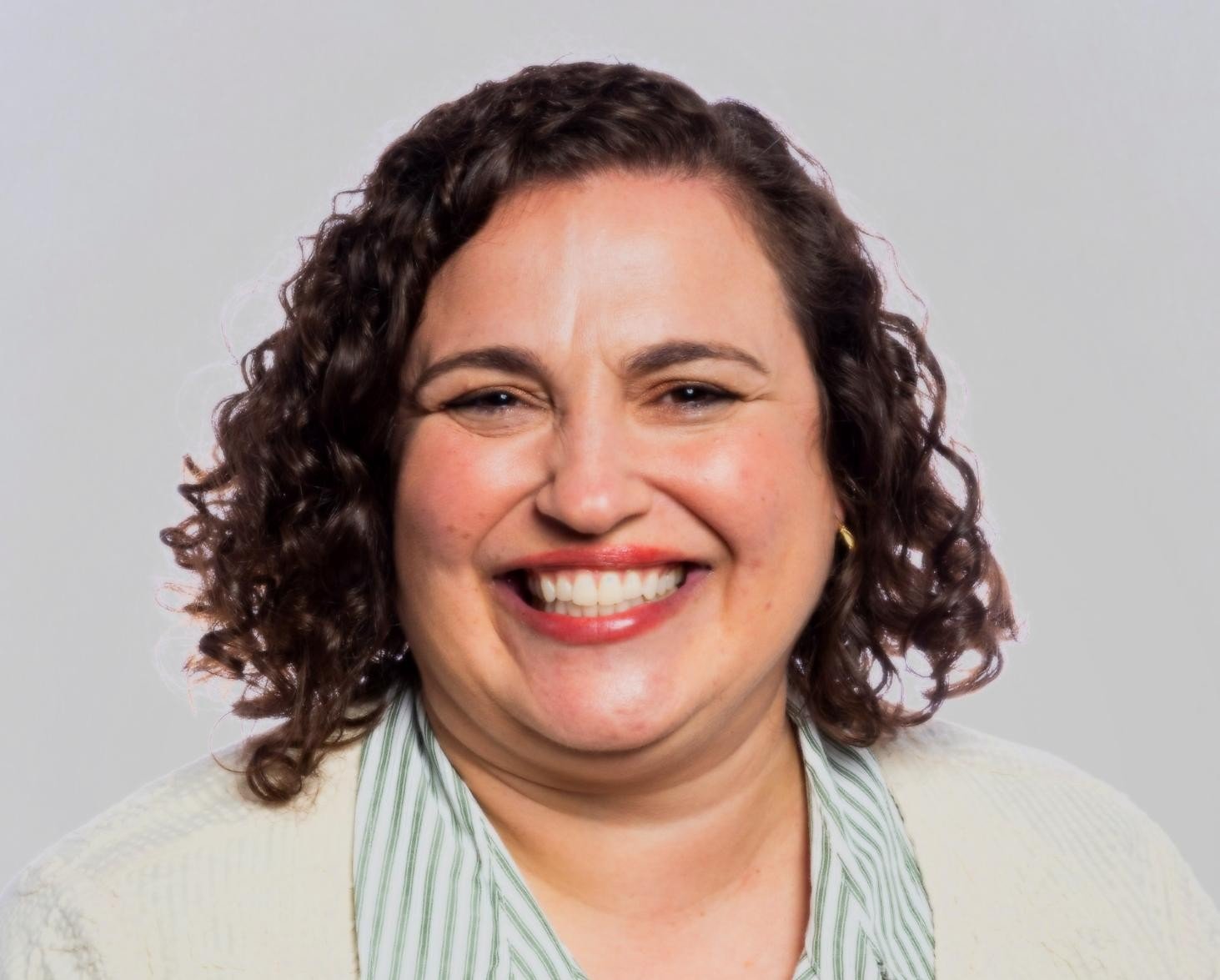 A smiling woman with curly dark hair against a white background