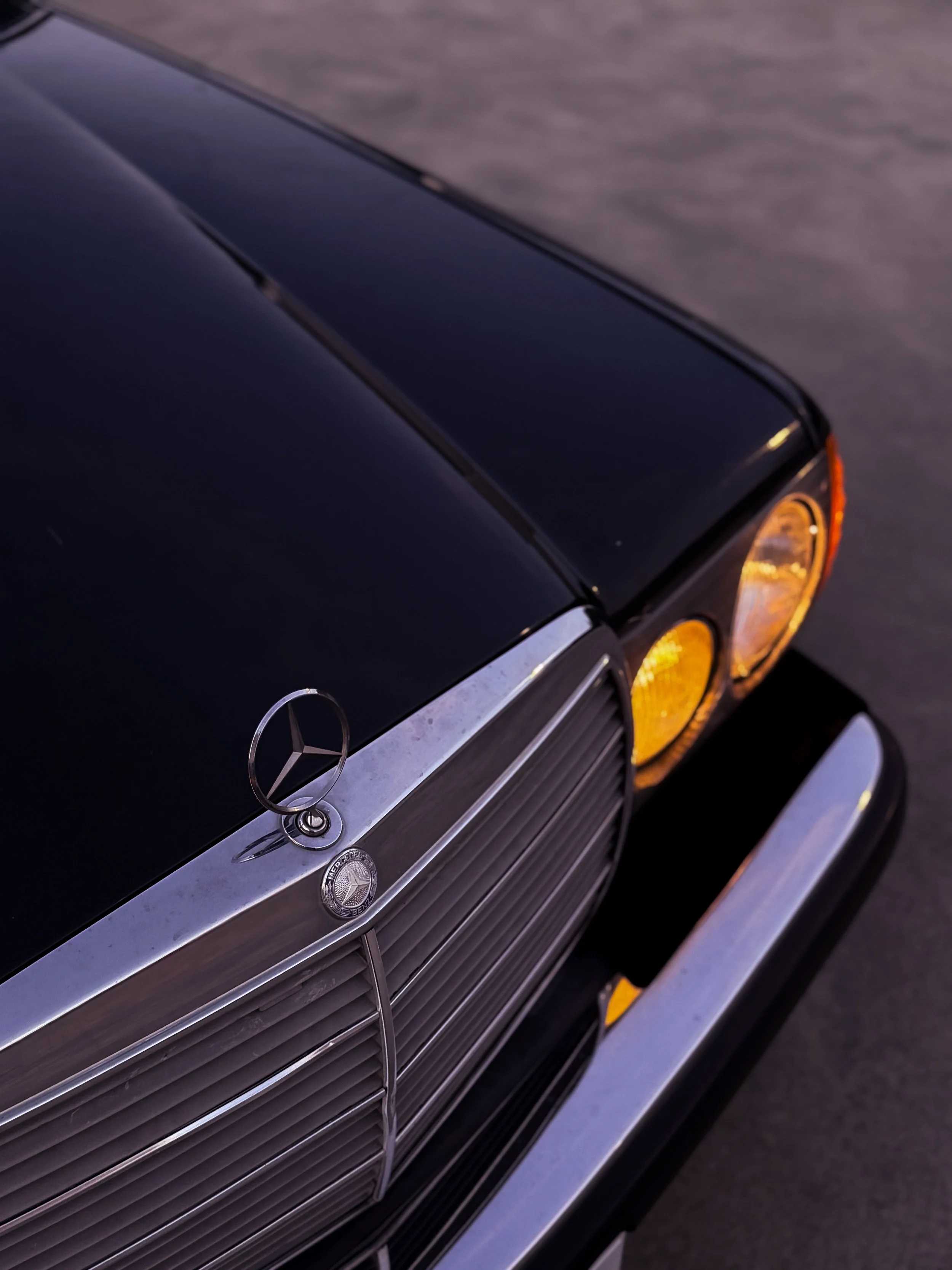 Close-up of the front part of a vintage black Mercedes-Benz car, displaying the grille, badge, and yellow headlights.