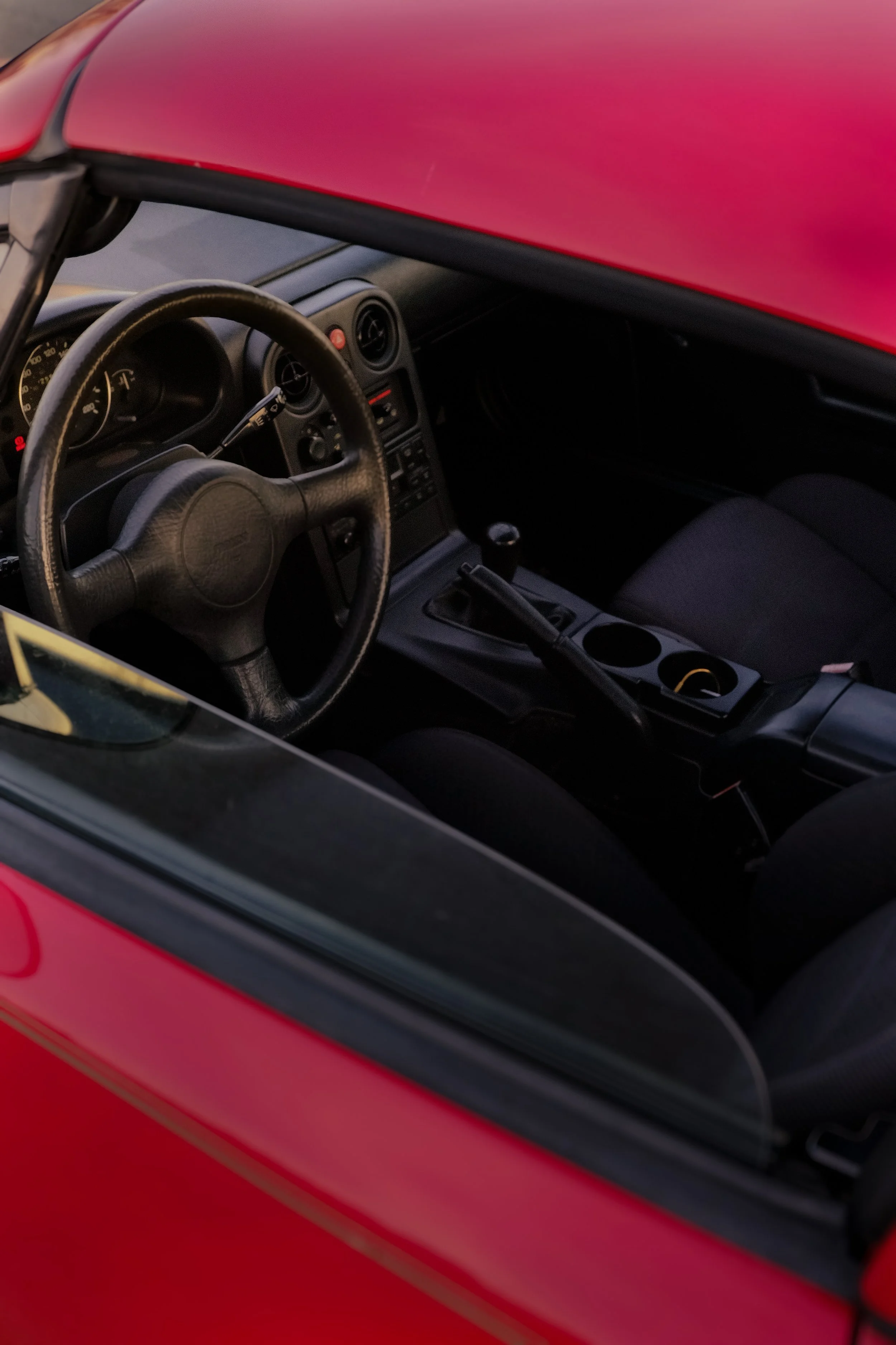 Interior of a red sports car showing the steering wheel, dashboard, and center console with cup holders.