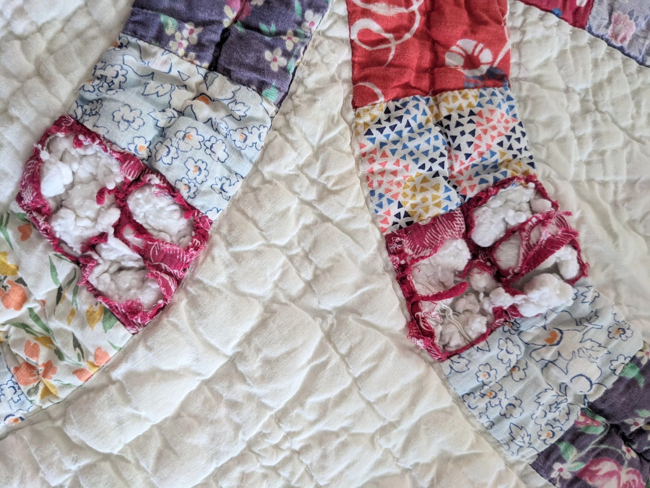 Close-up of a patchwork quilt with various colored and patterned fabric squares, some with floral designs, and edges with pink and red stitching.
