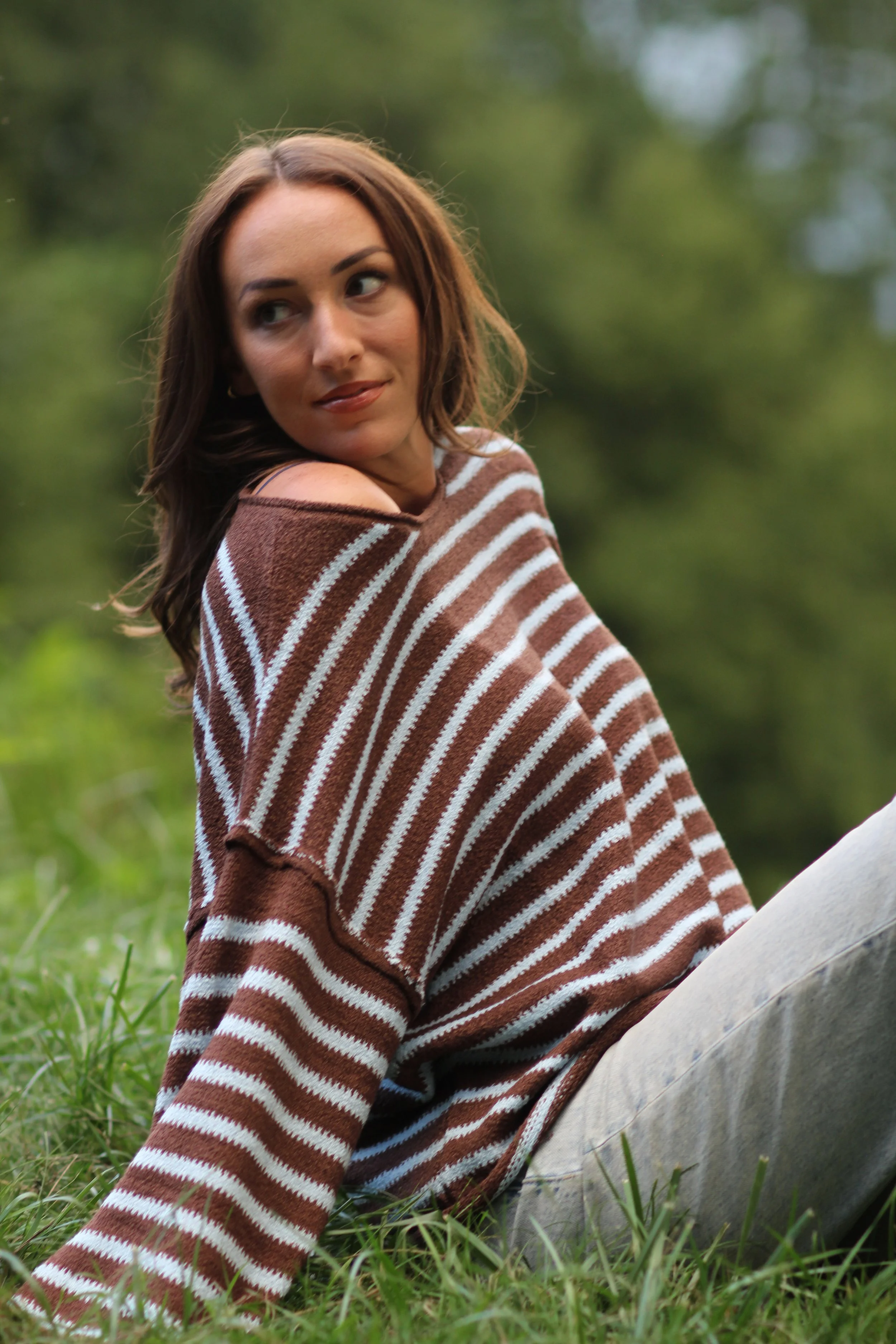 Woman standing outdoors in a wooded area wearing the Fireside Stripe Sweater and jeans, front view